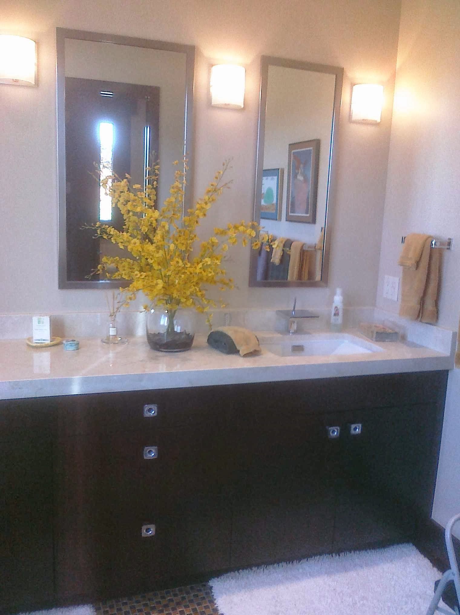 Bathroom vanity with dark brown cabinets, light countertop, two mirrors, and yellow flowers.