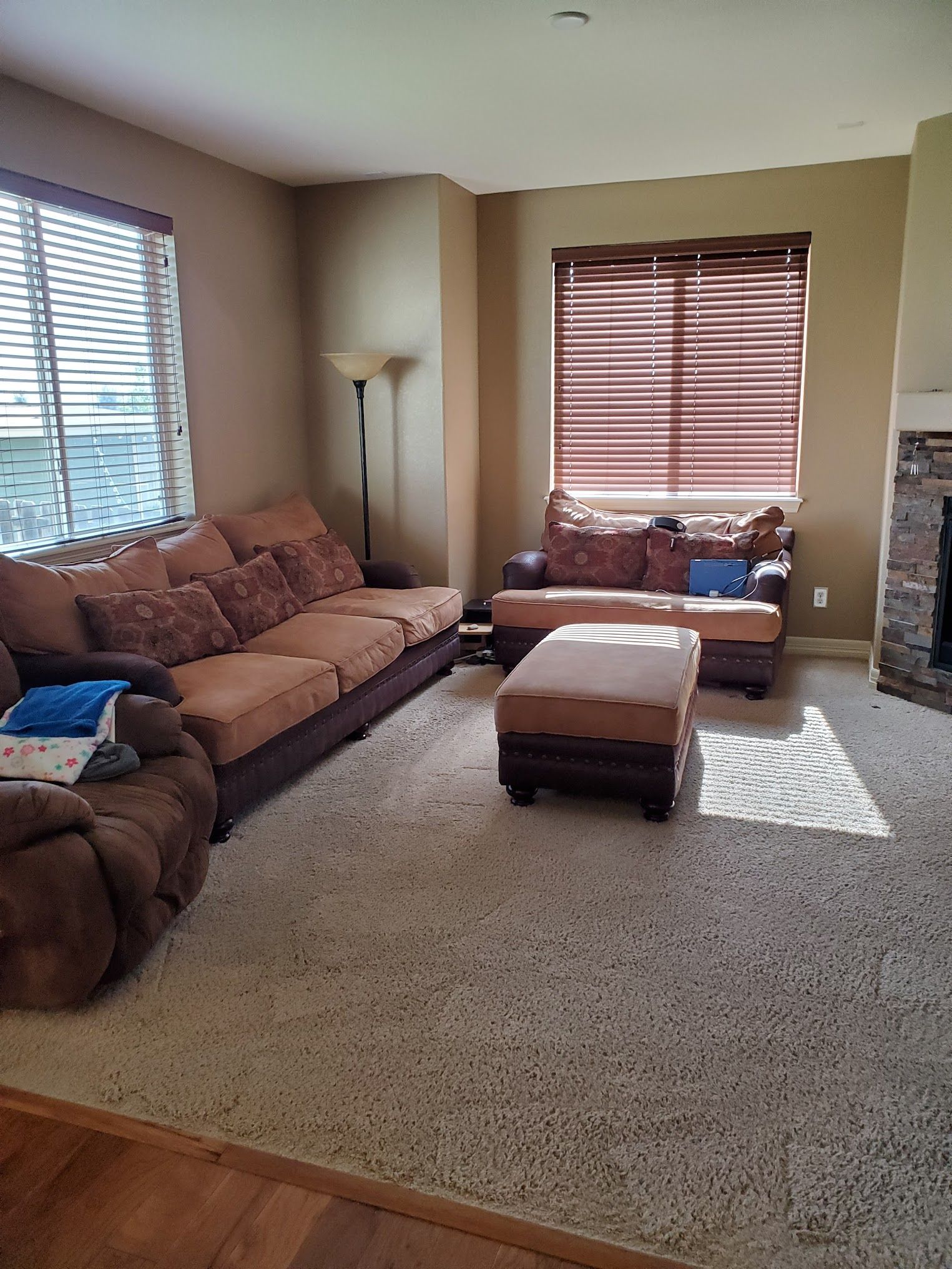 Living room with brown and tan furniture, beige carpet, and window blinds.