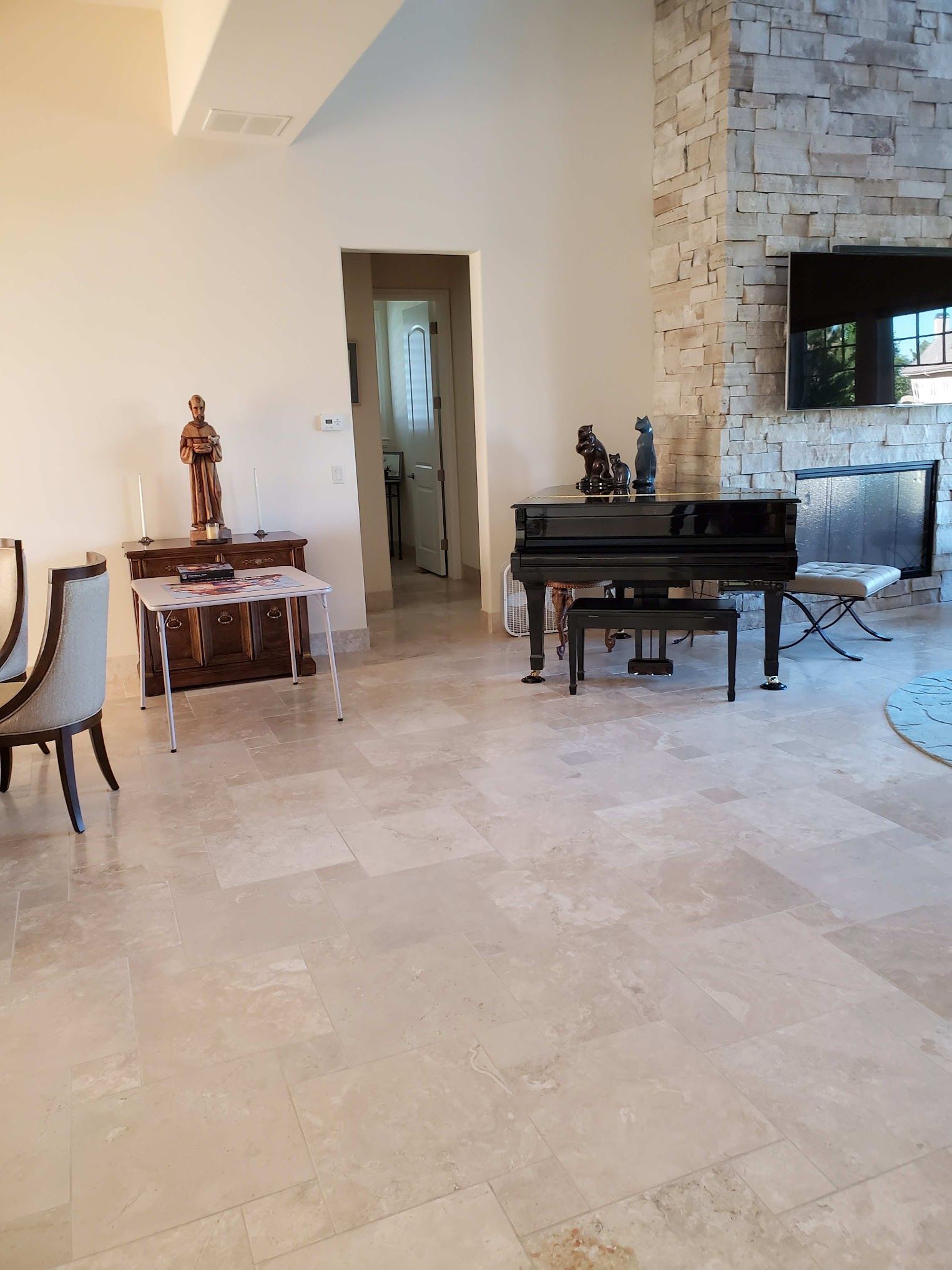 Living room with grand piano, fireplace, and doorway, with beige tile flooring.