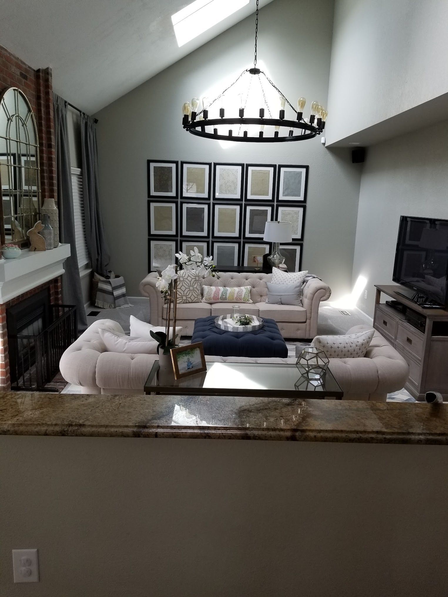 Living room with a beige tufted sofa, chairs, and a navy ottoman, framed pictures on the wall, and a chandelier.