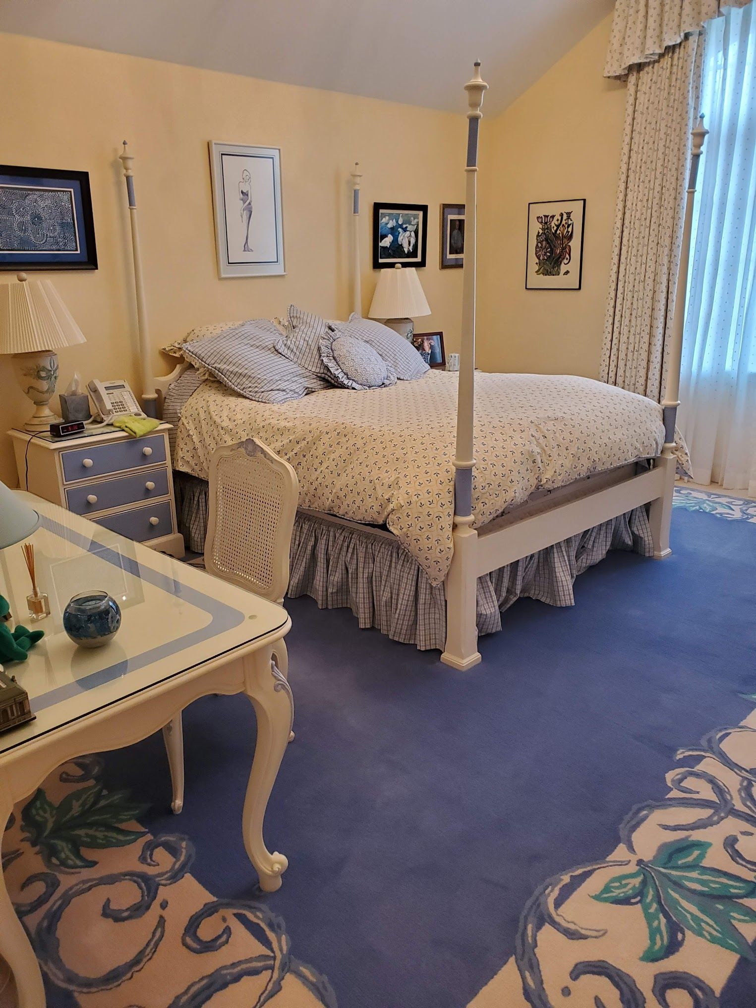 A bedroom with a four-poster bed, blue carpet, and pastel yellow walls.