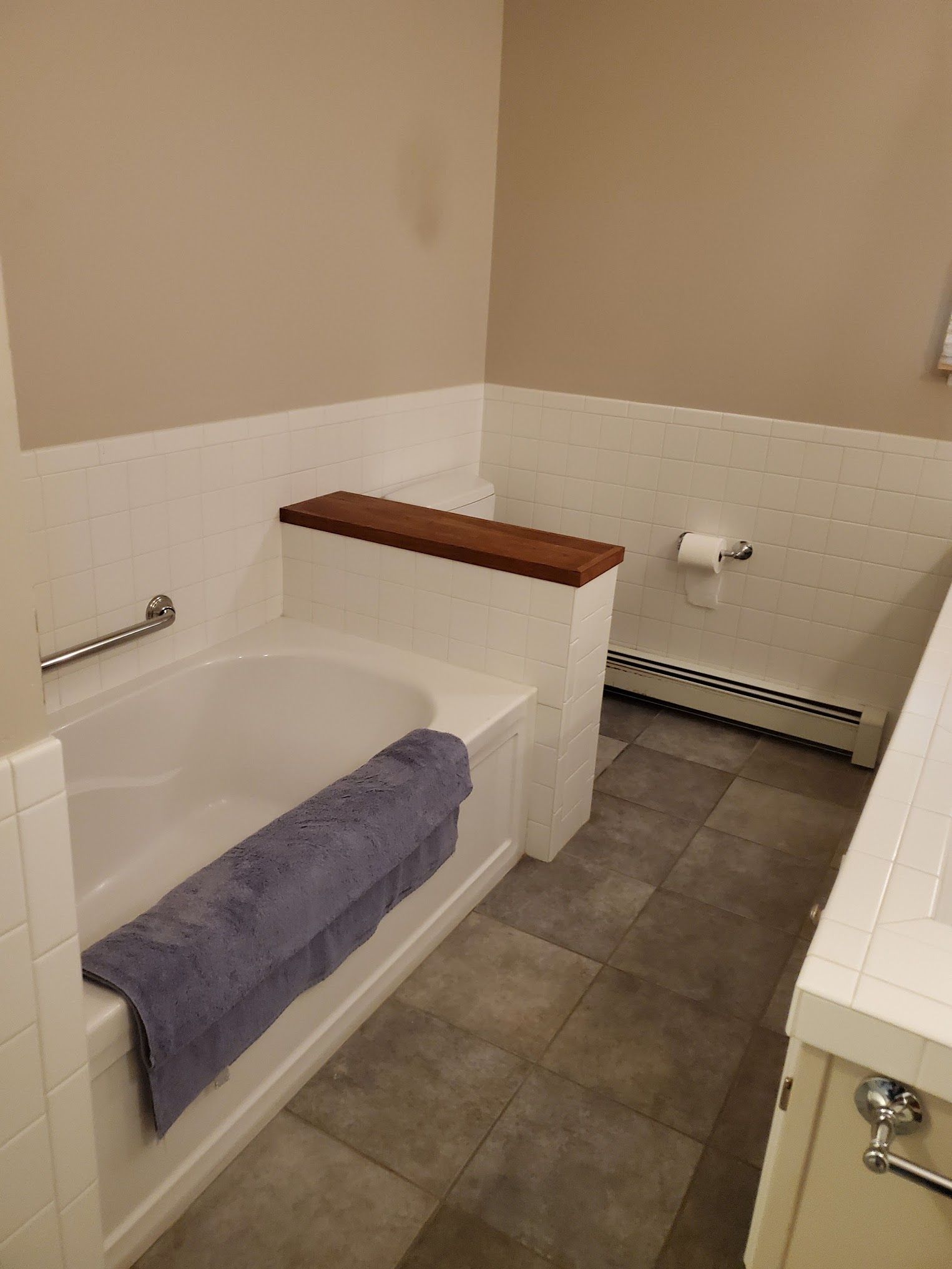 Bathroom with white tile, bathtub, and gray tile floor. A purple towel lies on the tub's edge.