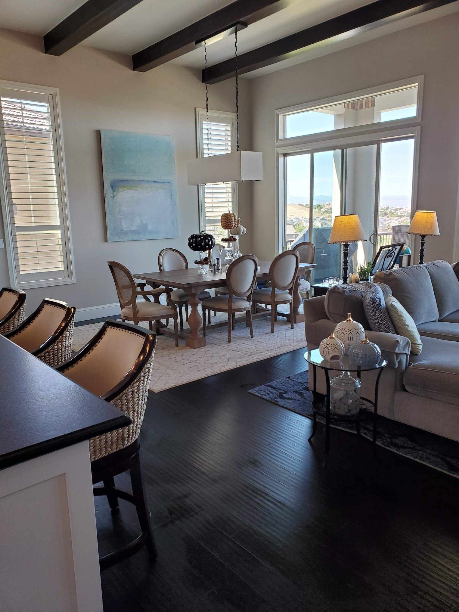 Spacious dining area with dark wood floors, a round table, and large windows, next to a kitchen with bar seating.