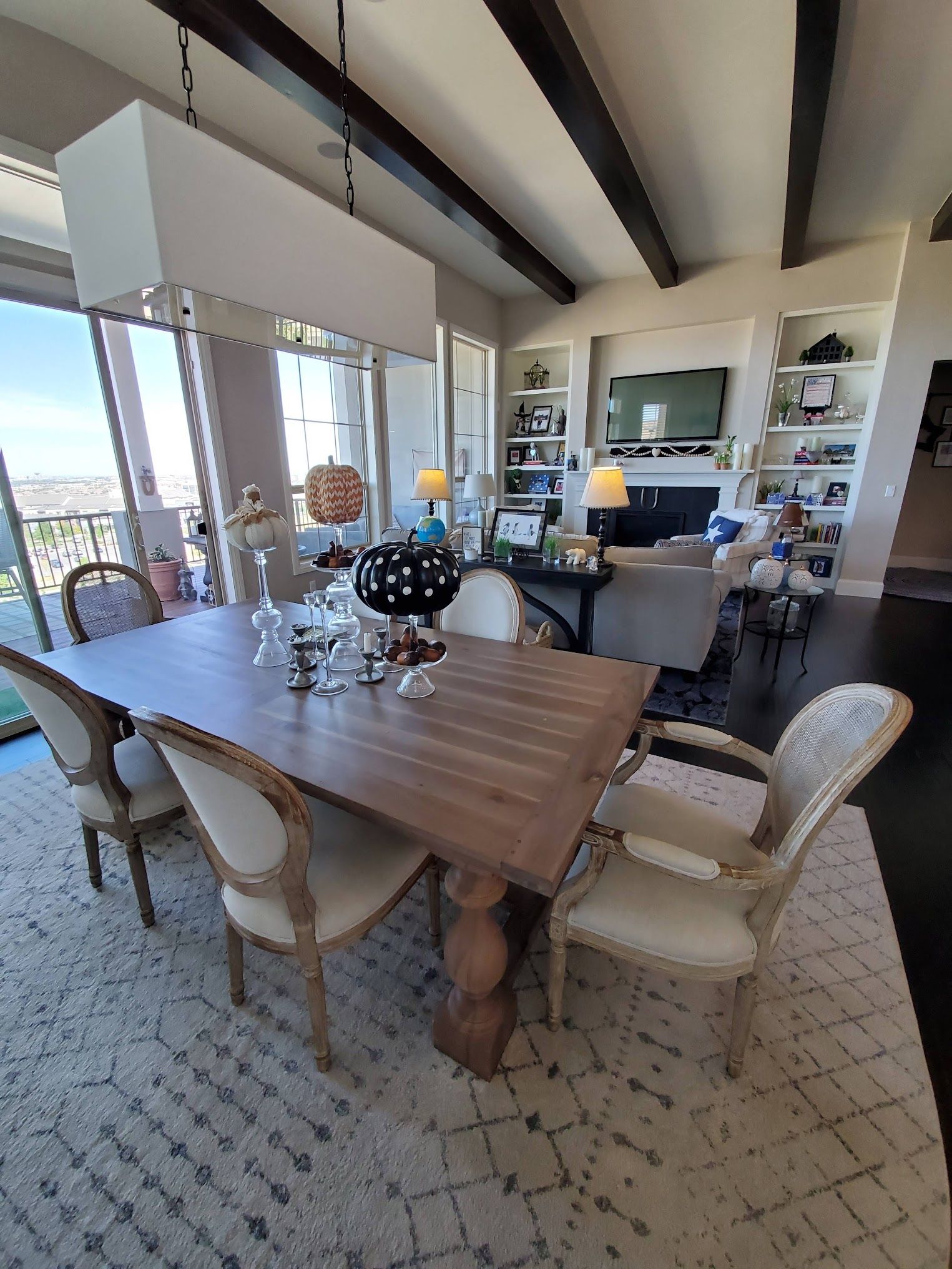 Dining room with wooden table and chairs, rug, large windows, built-in shelves, and decorative pumpkins.
