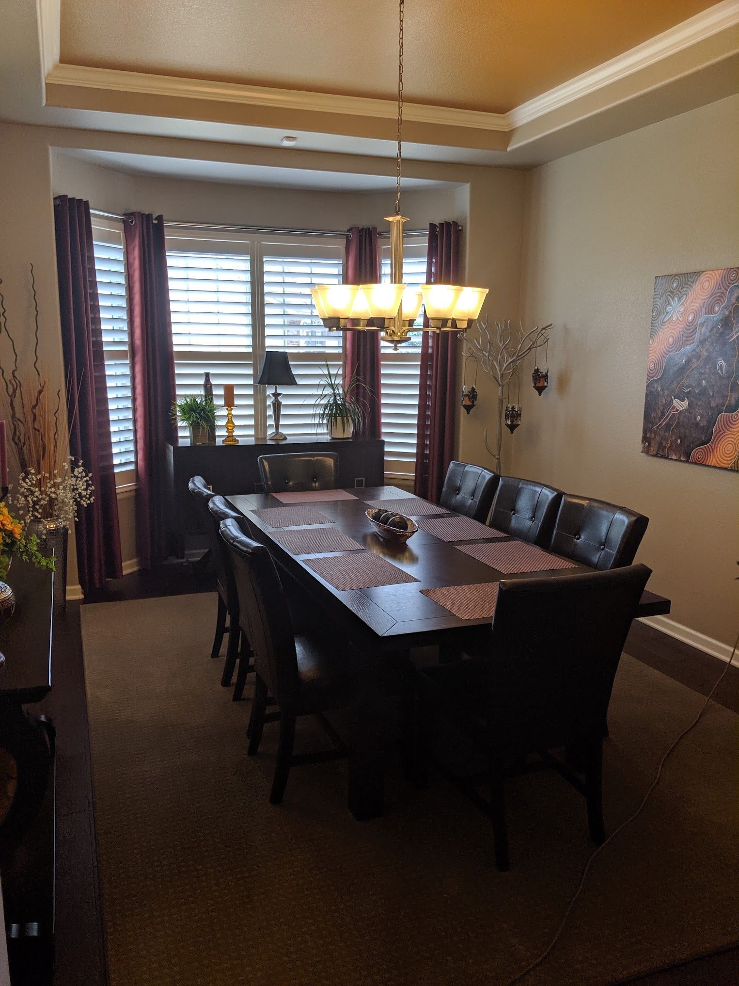 Dining room with a long table, dark chairs, bay window, and chandelier.