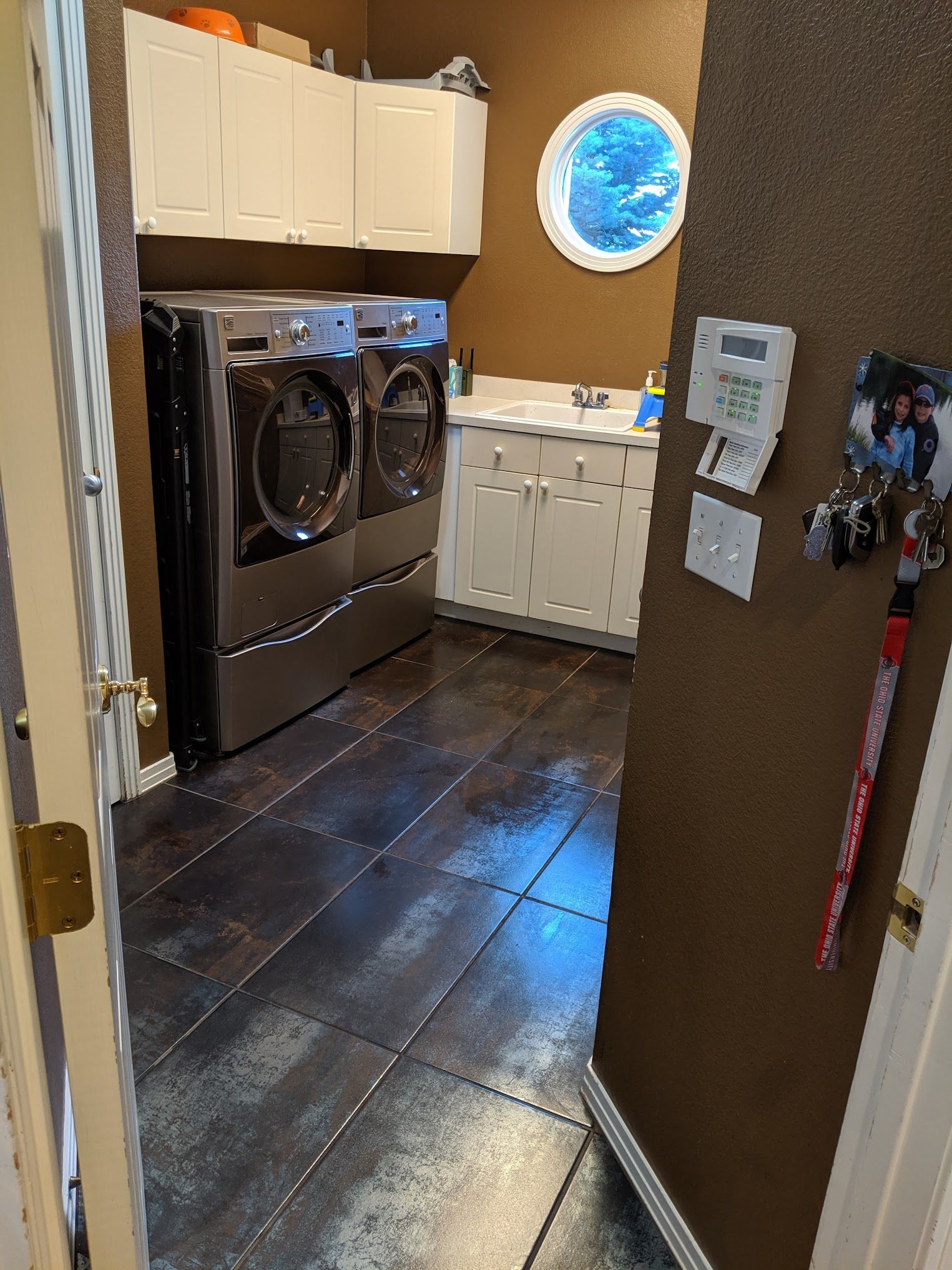 Laundry room with washer/dryer, white cabinets, brown walls, and dark tiled floor.