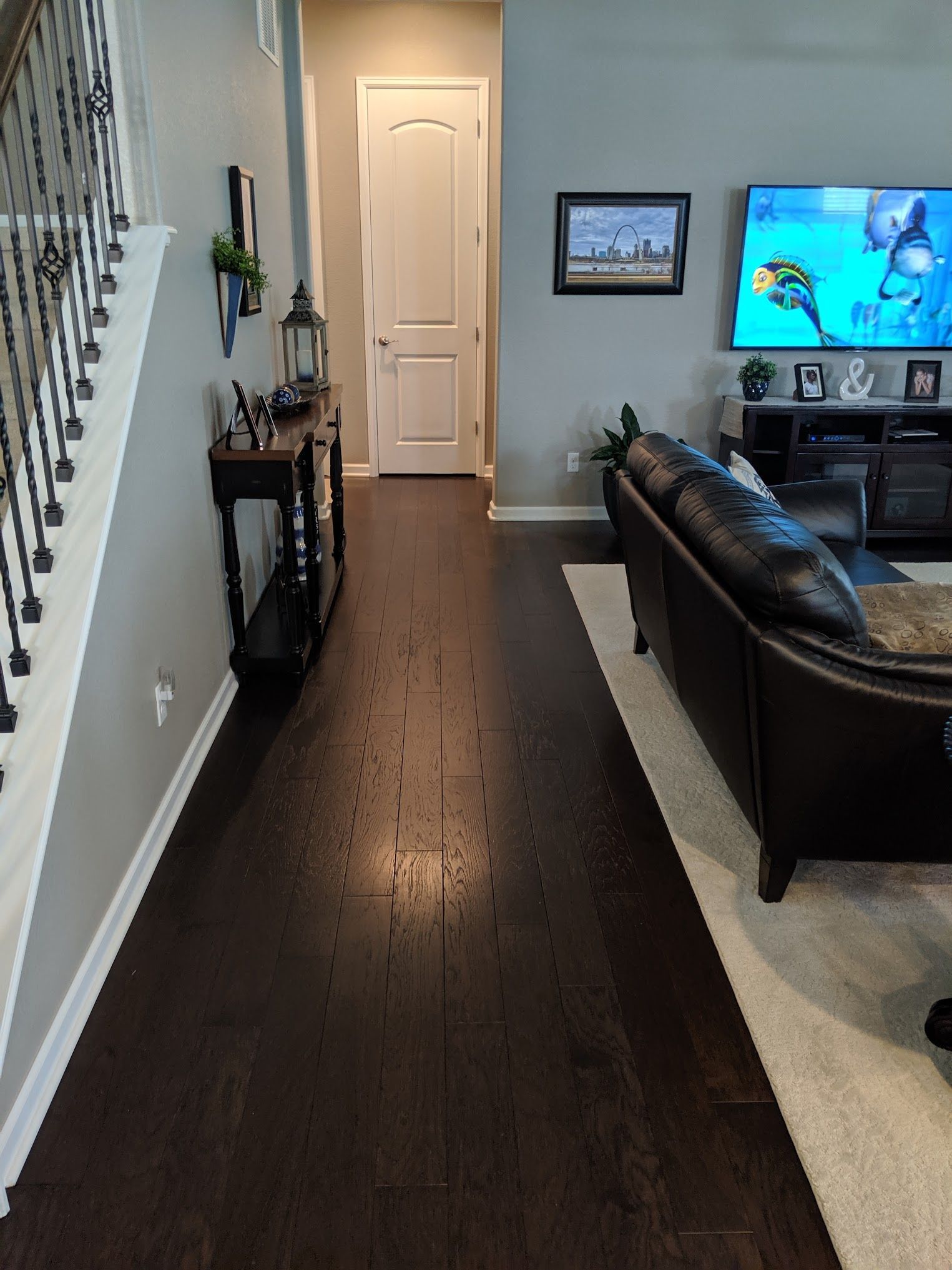 Hallway with dark wood flooring, staircase, console table, door, and living room with TV.