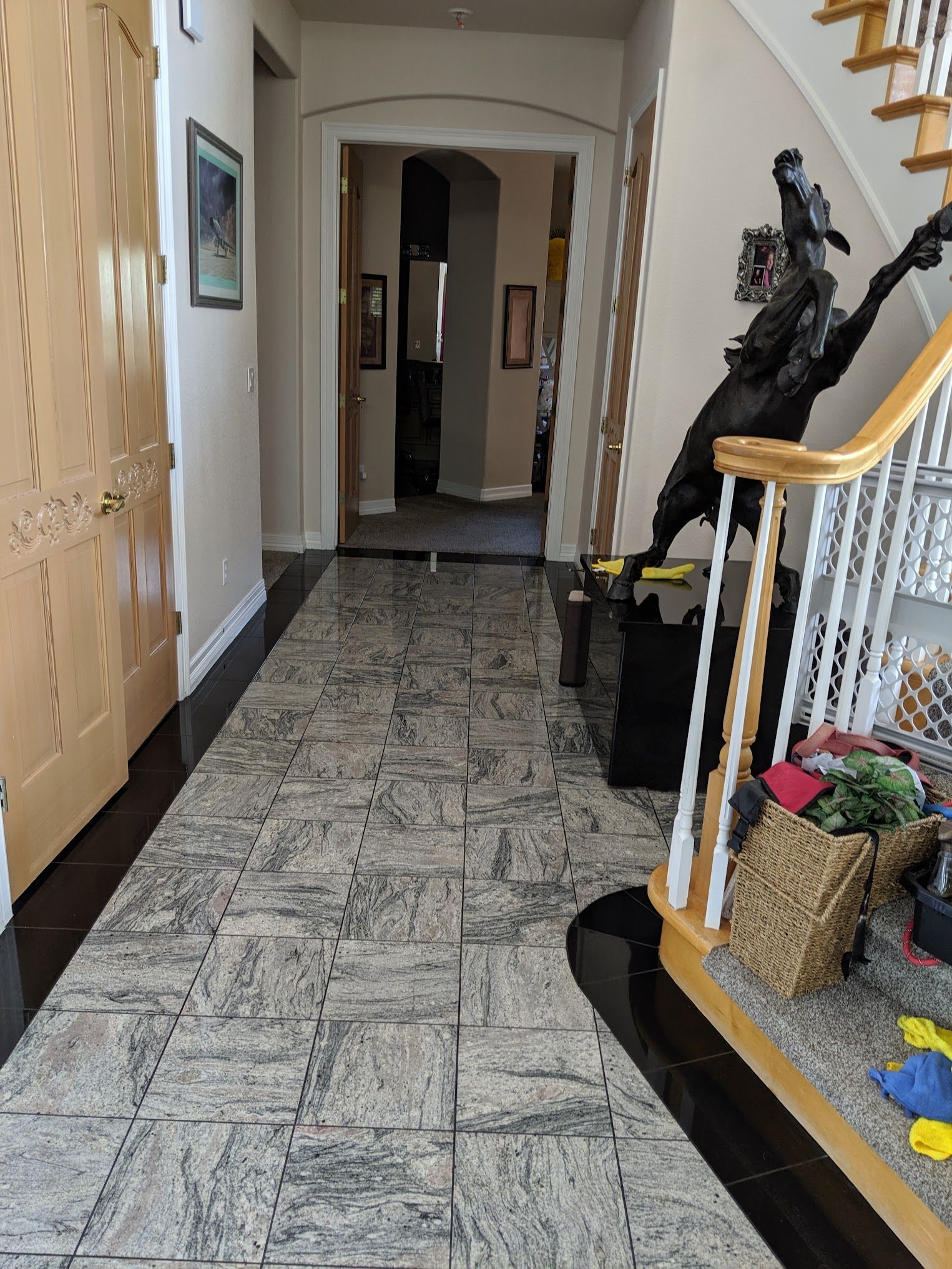 Hallway with patterned tile floor leading to another room, stairs with black sculpture on right.