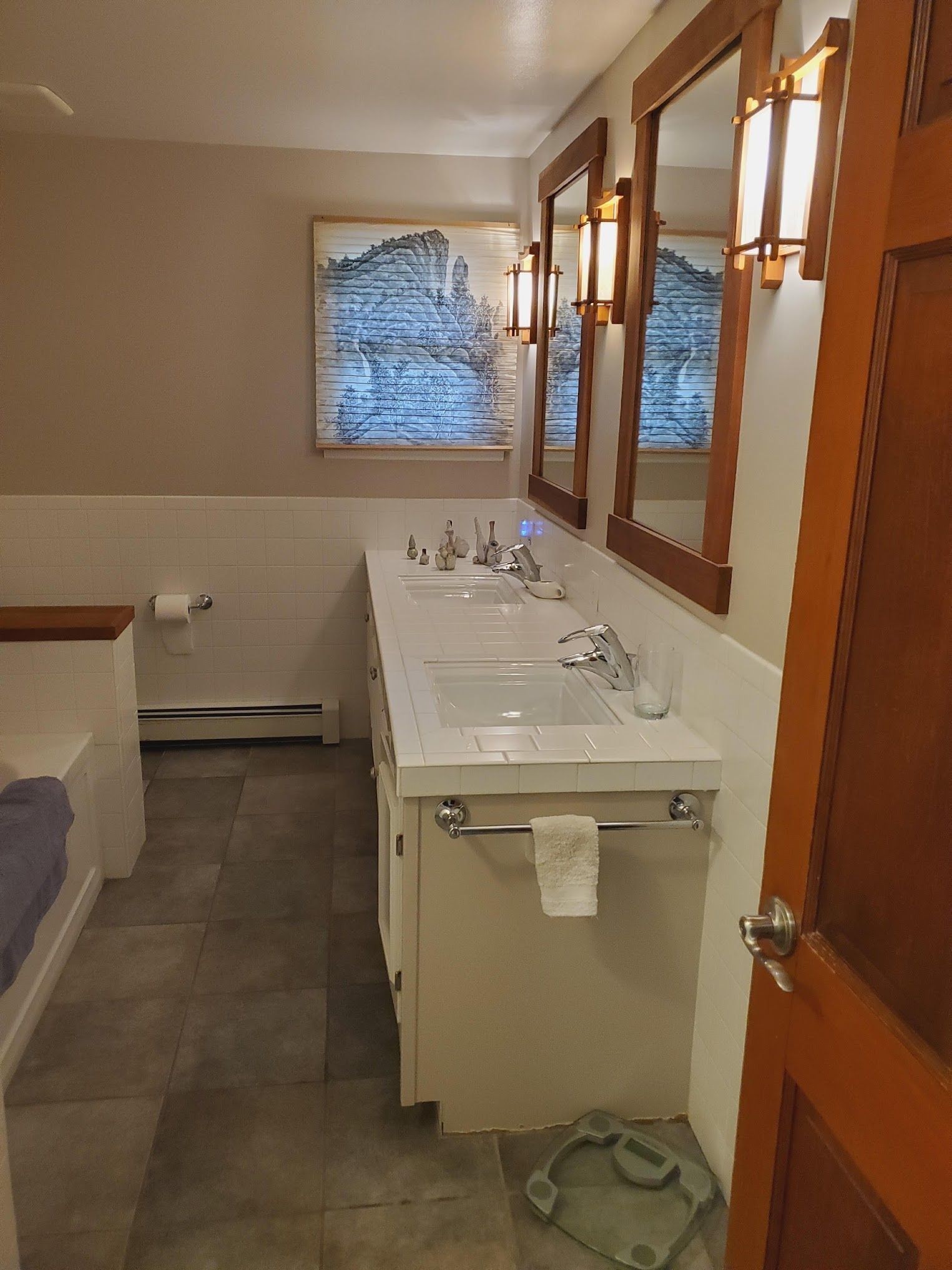 Bathroom with double sinks, mirrors, and a framed art print. Beige walls and wooden accents.