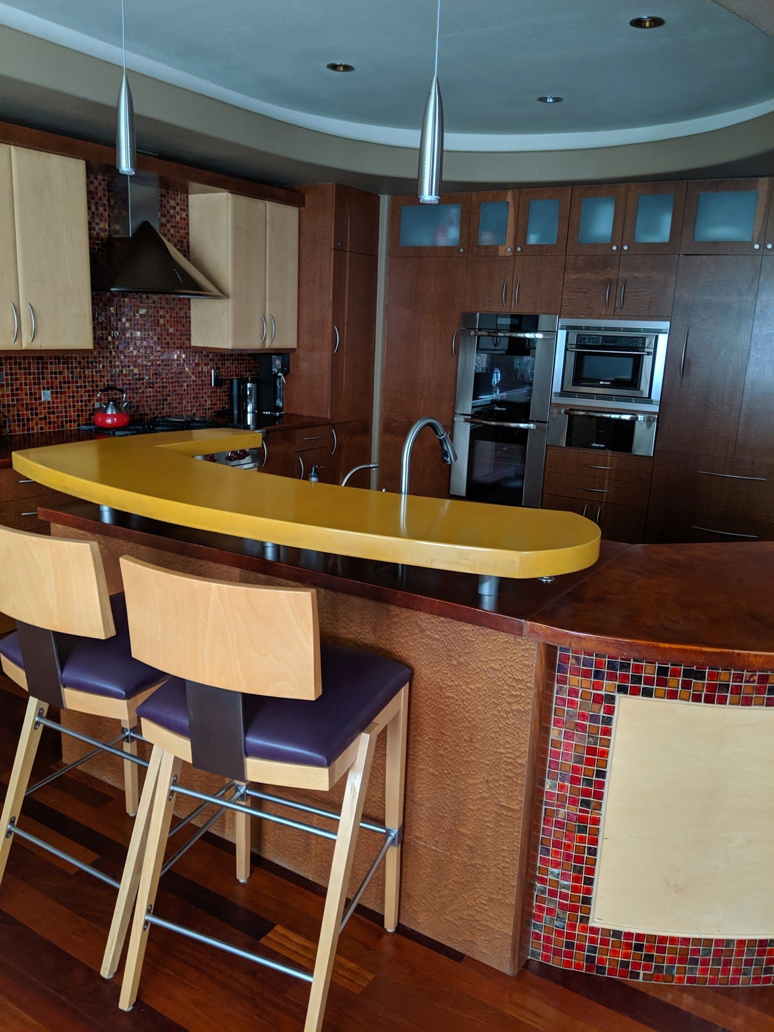 Kitchen with yellow countertop, bar stools, mosaic tile, and stainless steel appliances.
