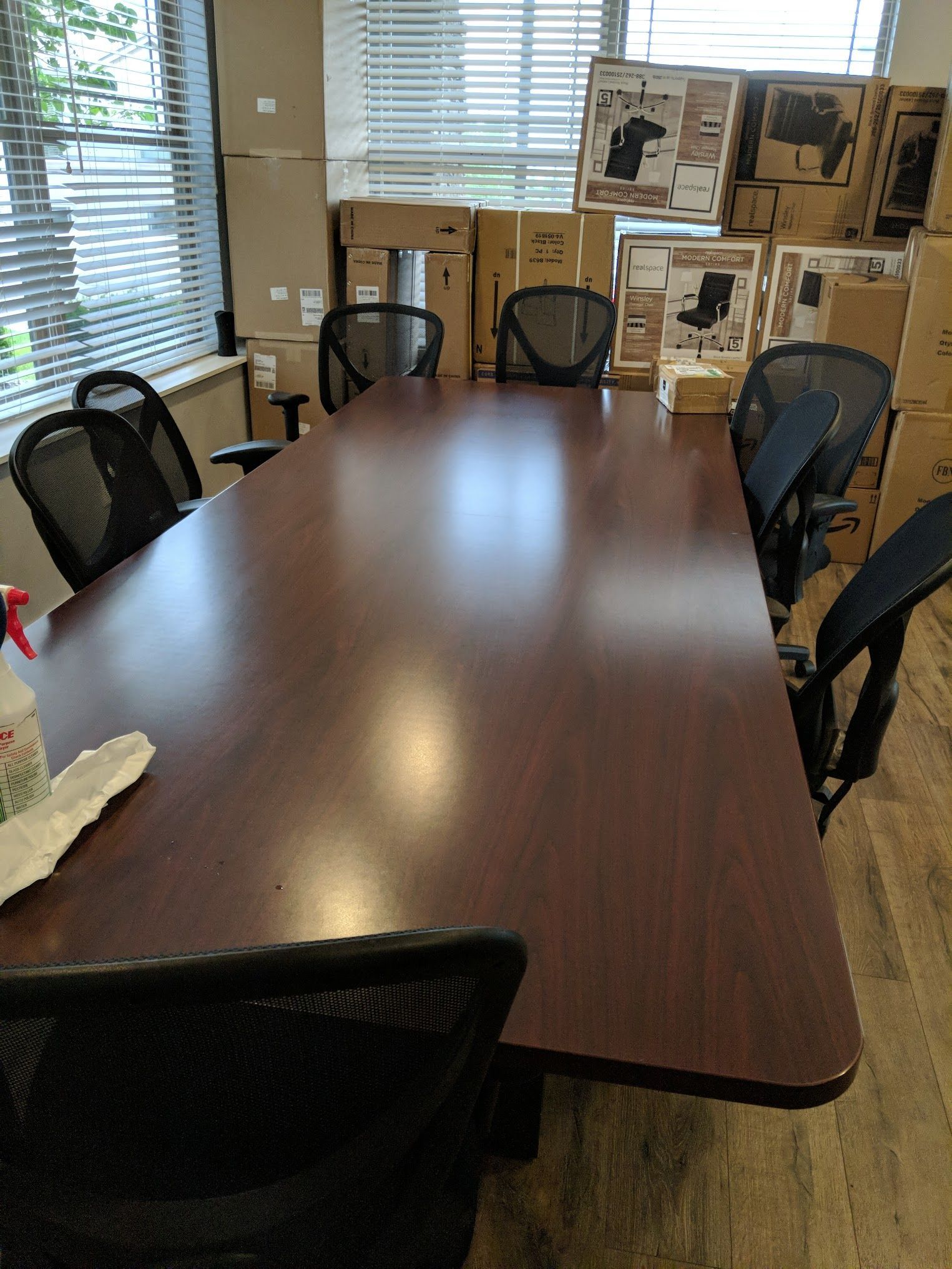 Conference room with dark wood table and black chairs. Boxes stacked in the background near a window.