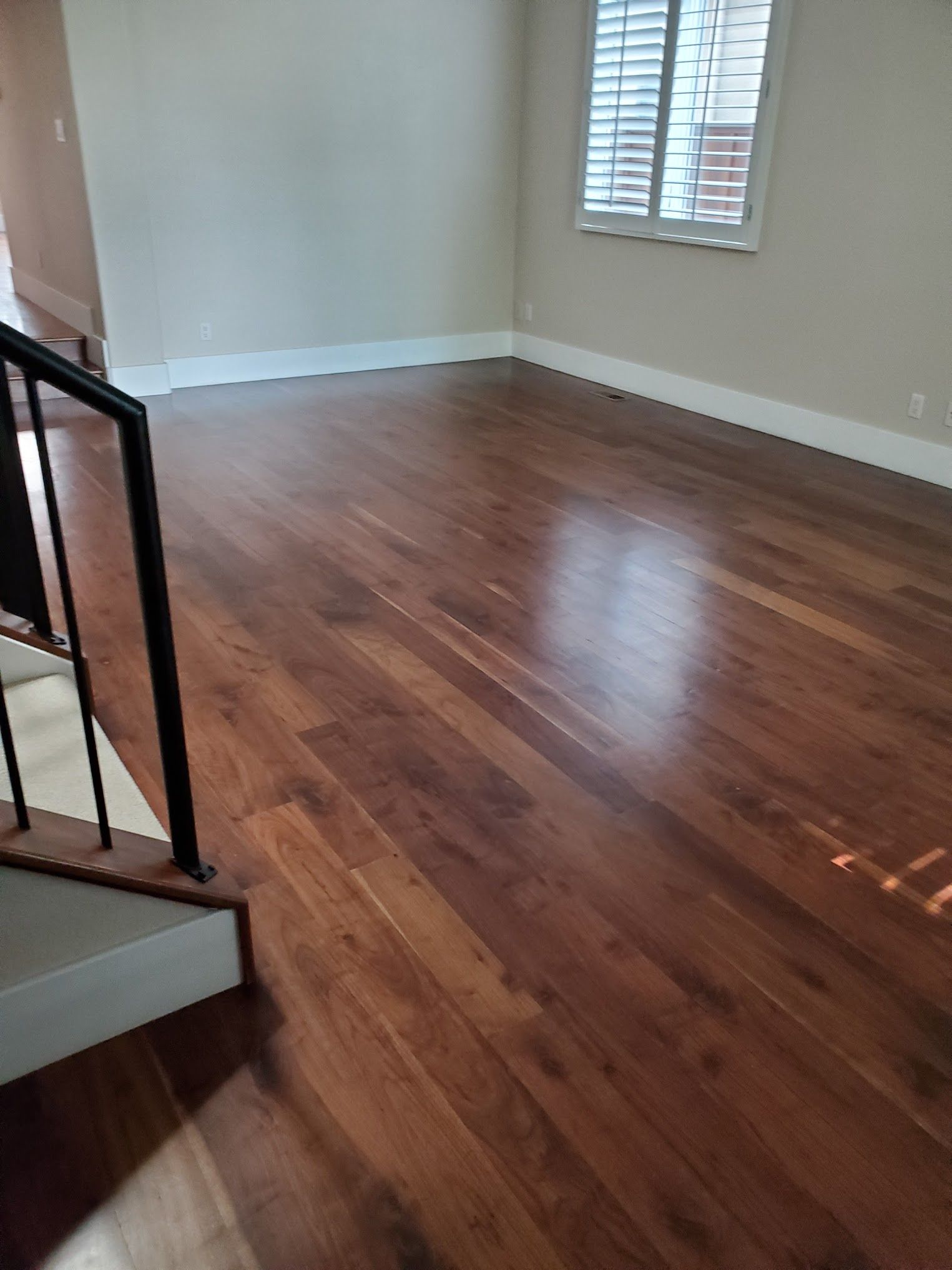 Hardwood floors in a room with a white baseboard and a window with white shutters.