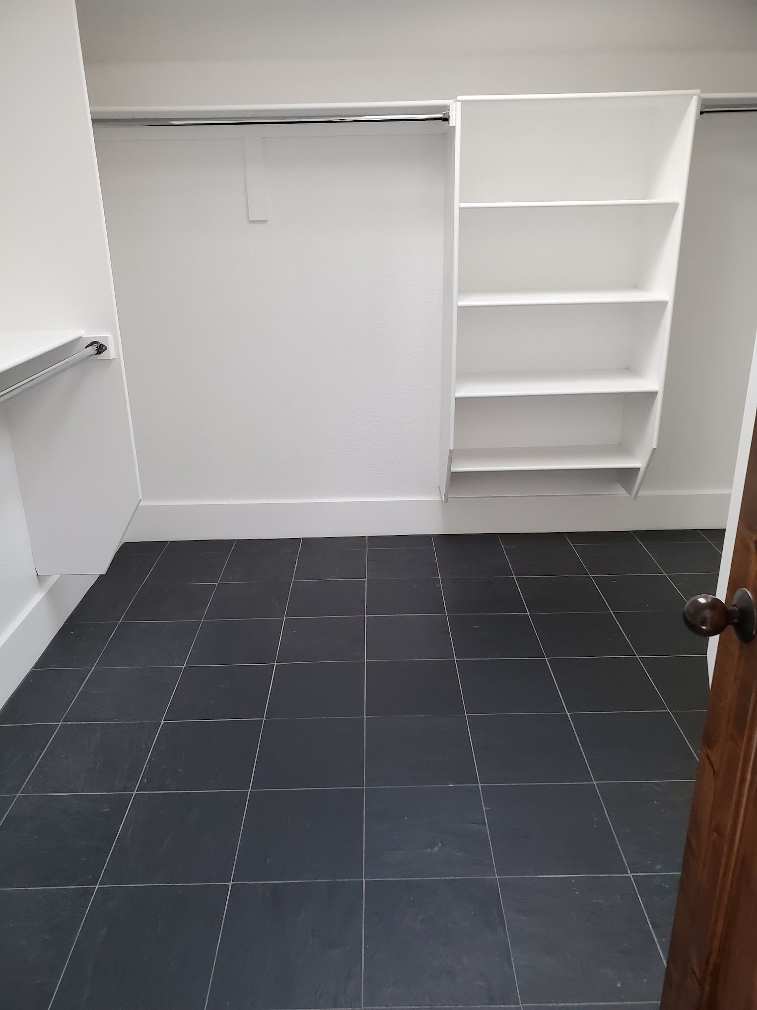 Empty white closet with black tiled floor; built-in shelves and clothing rod.