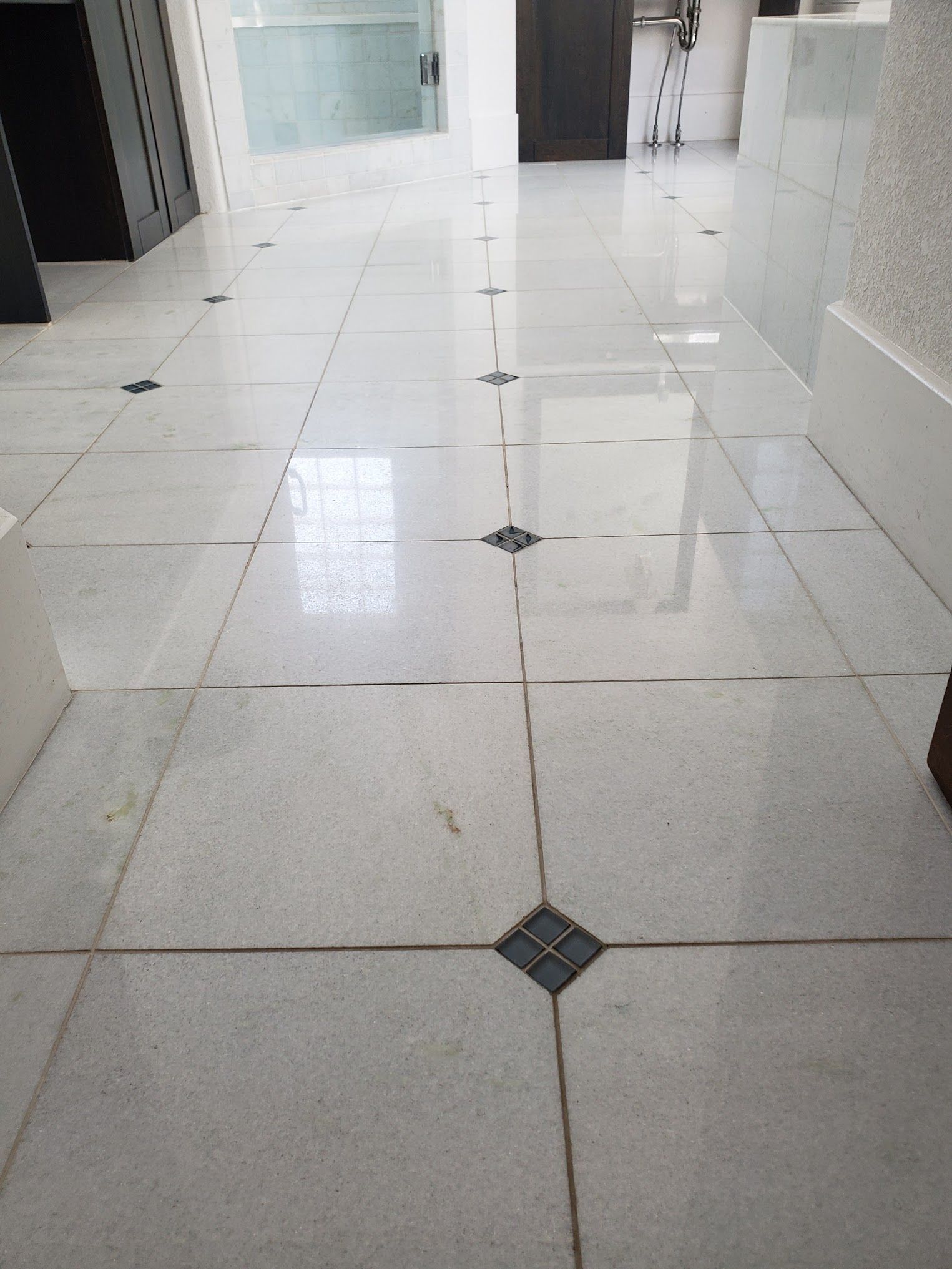 White tiled floor with dark diamond accents, leading toward a doorway.