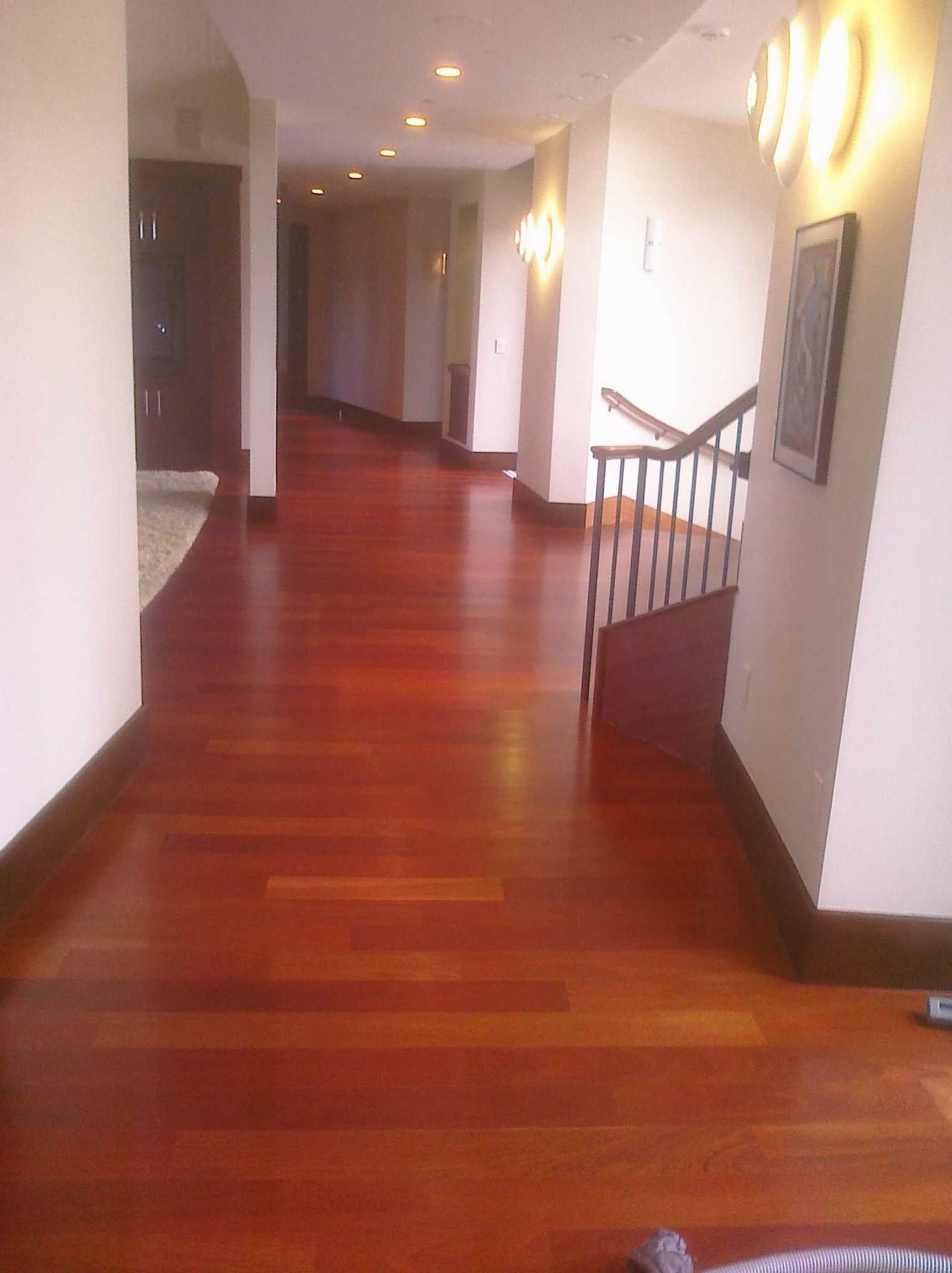 Long hallway with polished red wood floor, white walls, and recessed lighting. Staircase visible on the right.