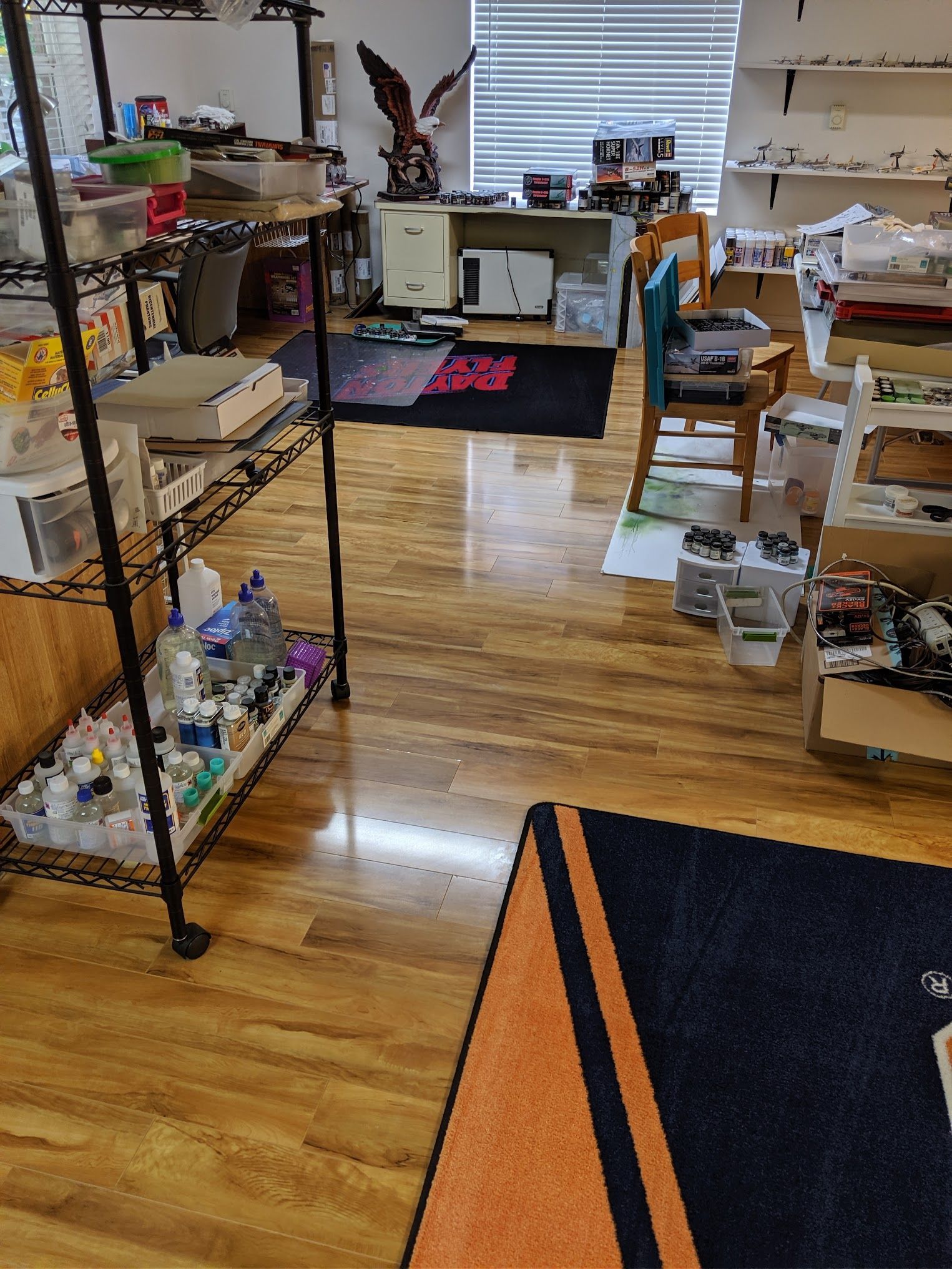 A room with wood floors, a shelving unit, and a desk.  Rugs on the floor.
