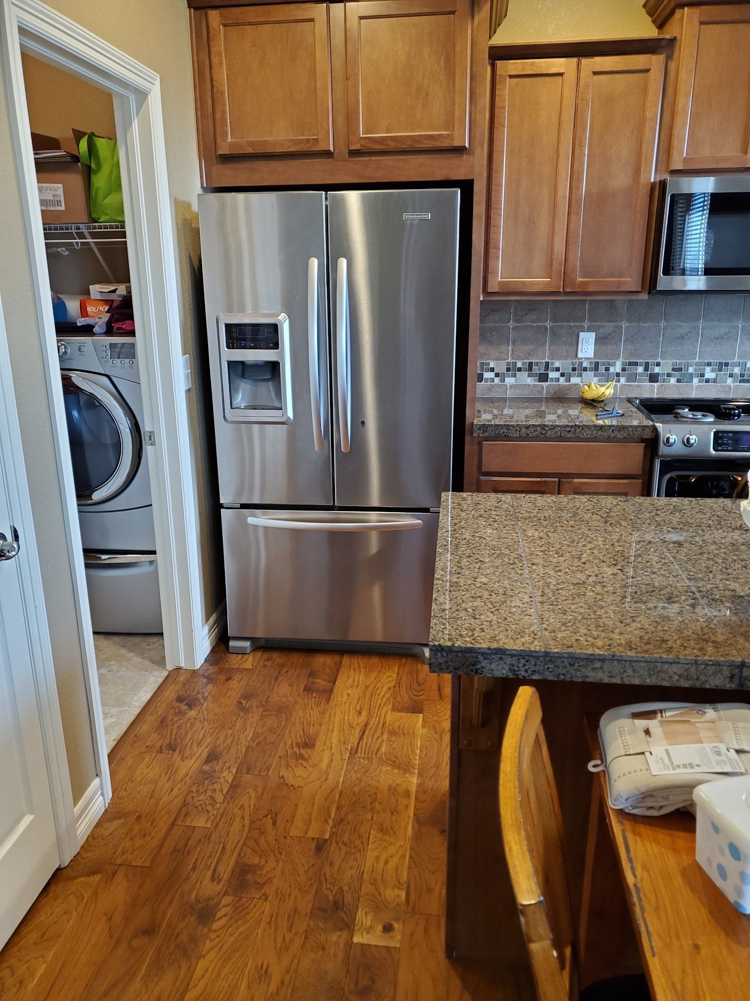 Stainless steel refrigerator in a kitchen with wooden cabinets and a pantry on the left.