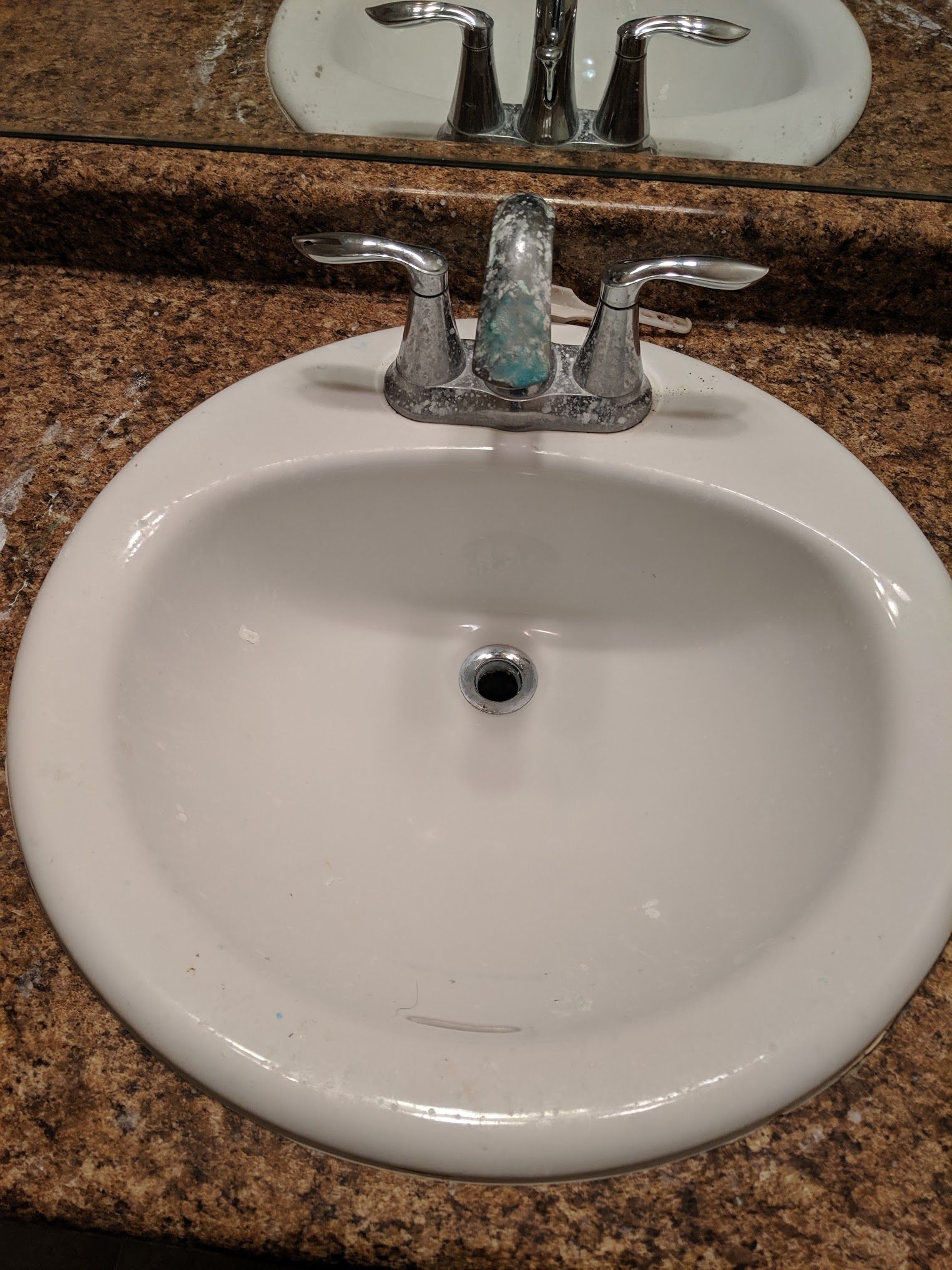 White bathroom sink with chrome faucet on a speckled brown countertop.