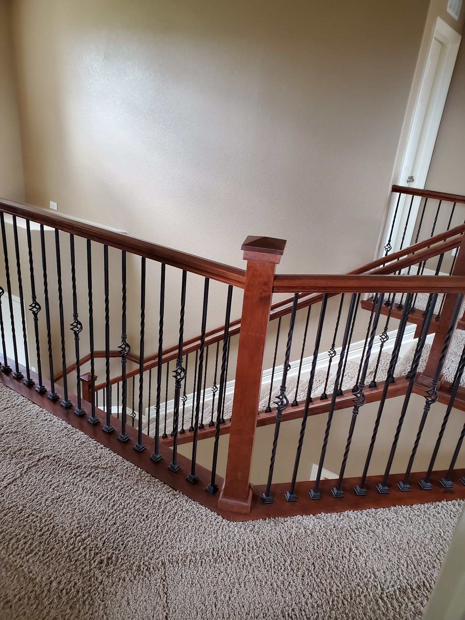 Wooden staircase with black iron railings, brown carpet.