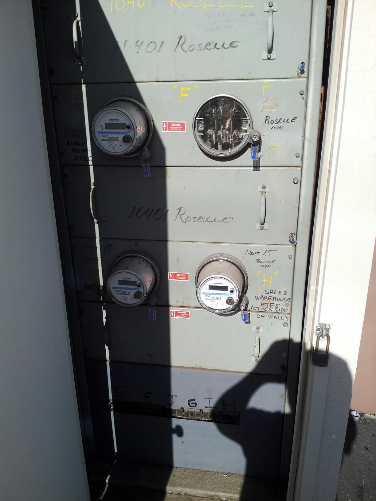 A shadow of a person is cast on a wall with electrical meters on it.