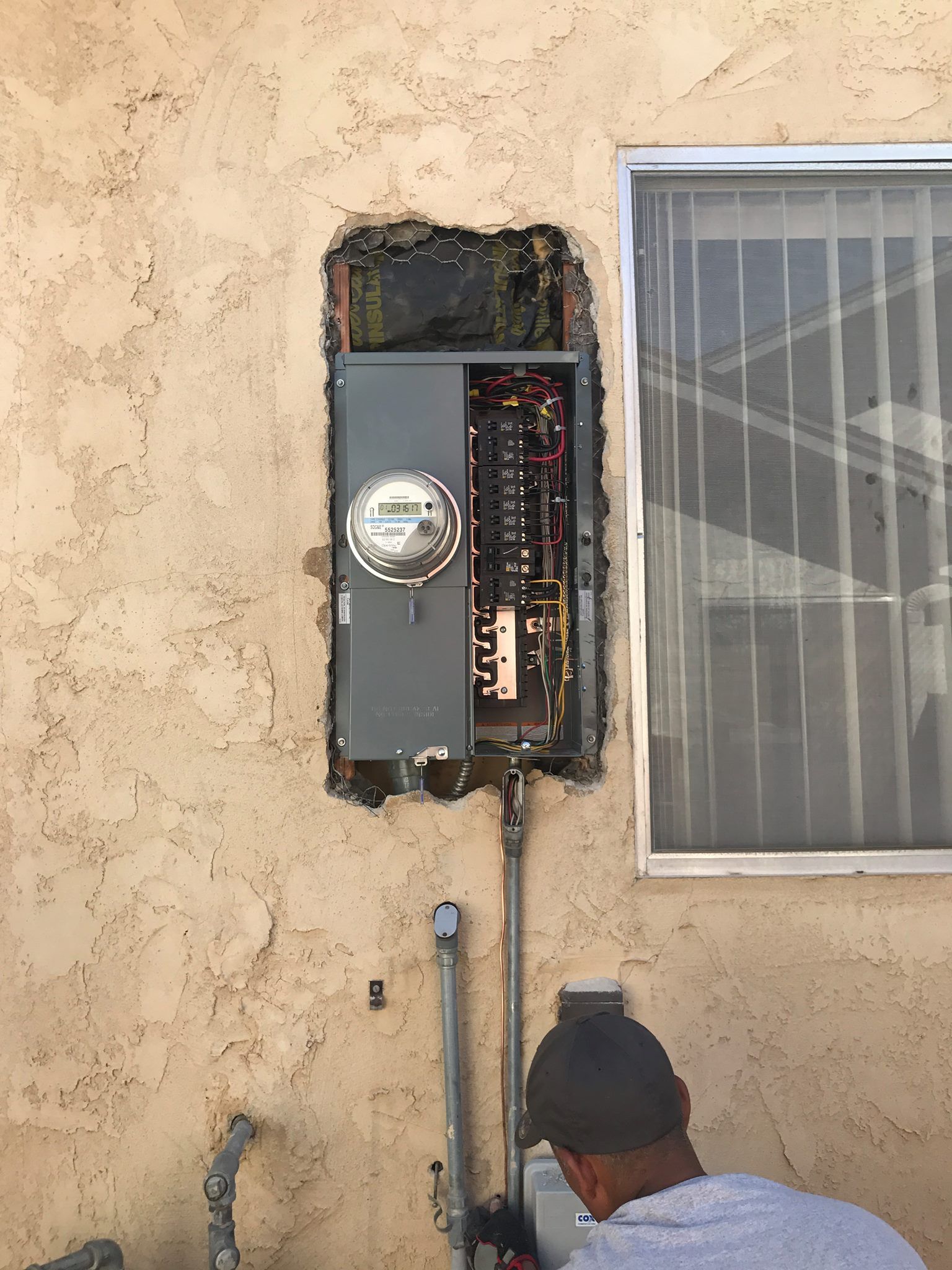 A man is working on an electrical box on the side of a building.