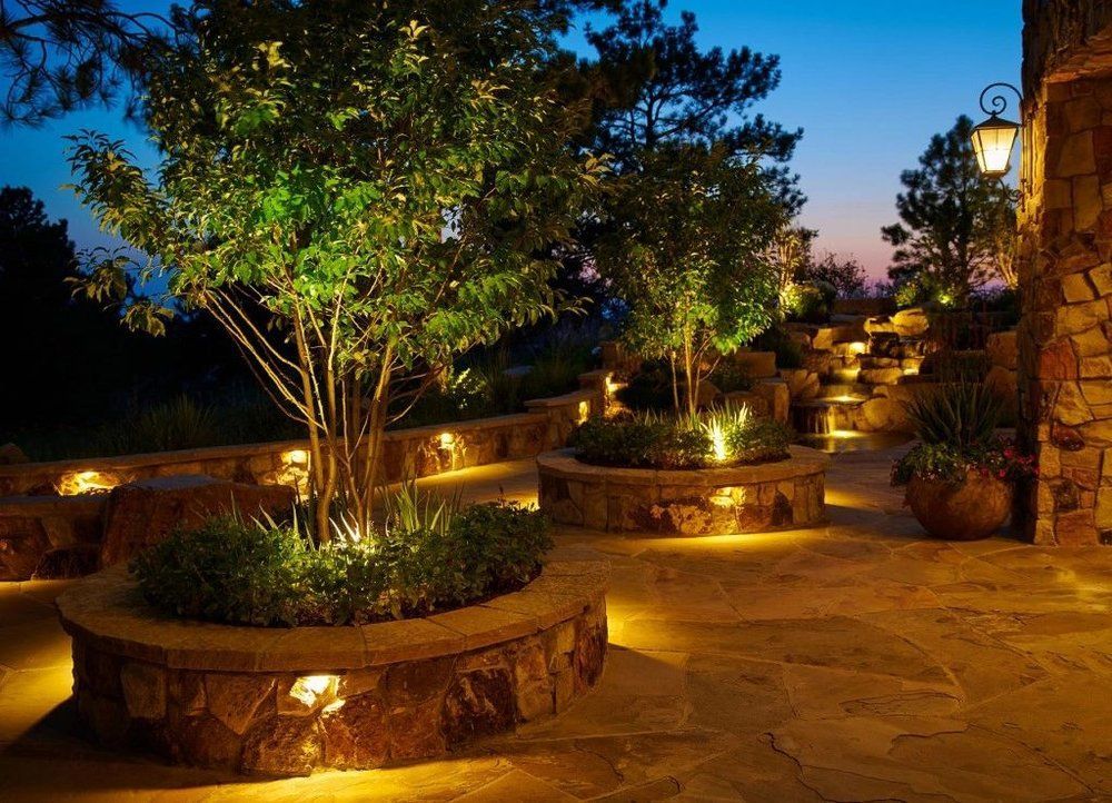 A patio with trees and bushes surrounded by lights at night.