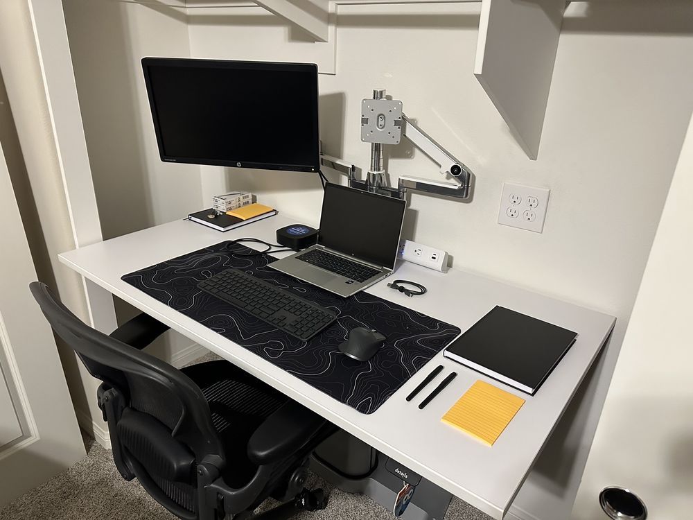 A desk with a laptop , monitor , keyboard , mouse and notebooks on it.