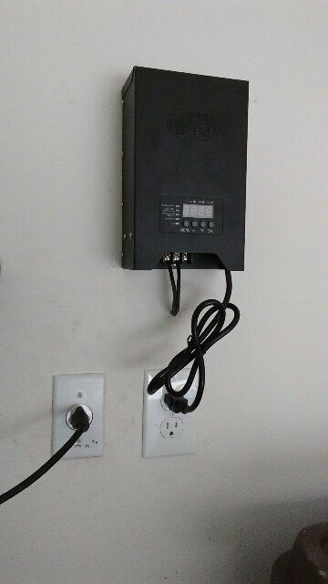 A black box with a cord attached to it is hanging on a wall.