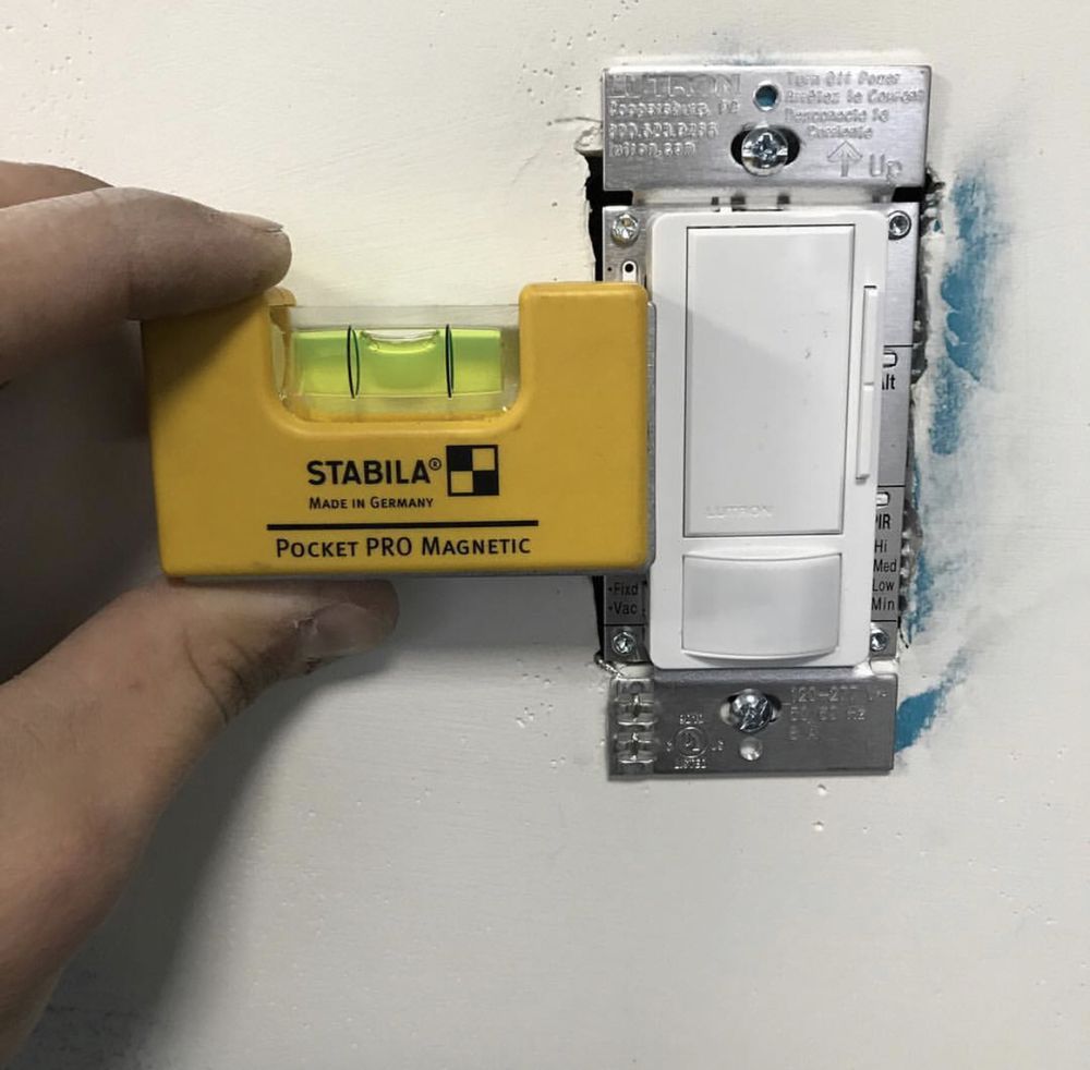 A person is measuring a light switch with a stabila pocket pro magnetic level