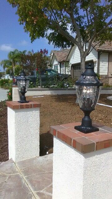 A couple of lights sitting on top of brick pillars in front of a house.