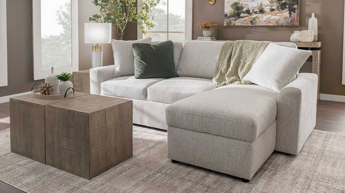 A living room with a white sectional couch , ottoman , and coffee table.