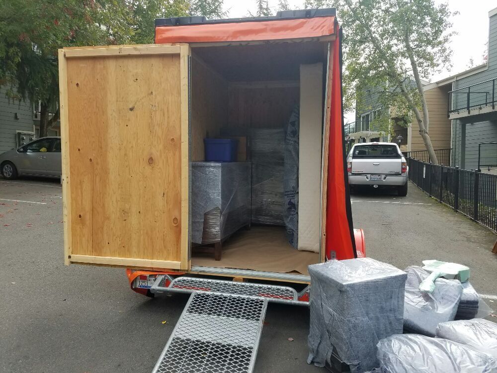 Orange moving trailer with ramp open; packed with furniture, in apartment parking area.