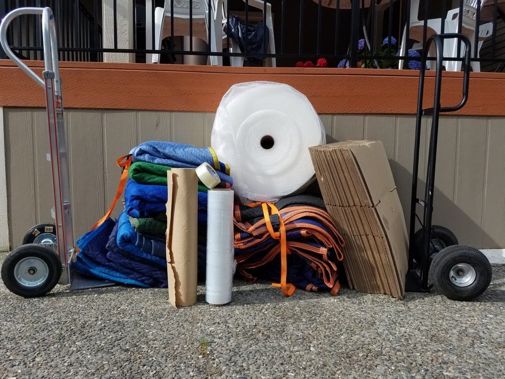 Two hand trucks flank a pile of moving supplies: blankets, bubble wrap, tape, and cardboard.