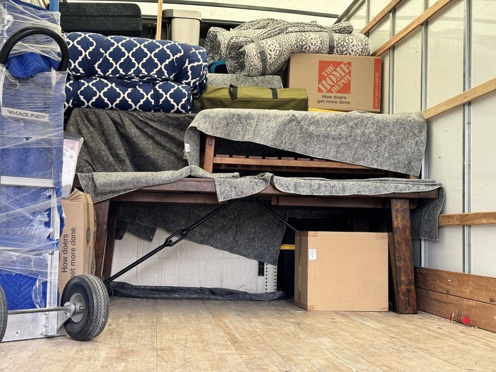 Inside a moving truck, various items are packed, including furniture, boxes, and cushions.