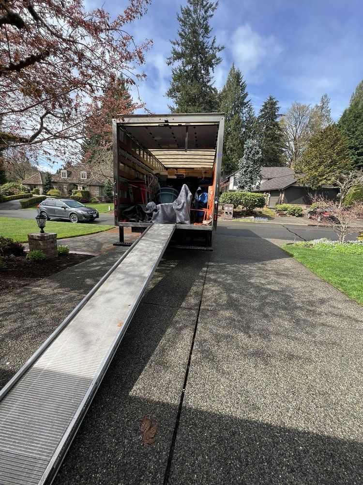 Moving truck parked in a driveway with ramp extended, ready for loading; sunny day.