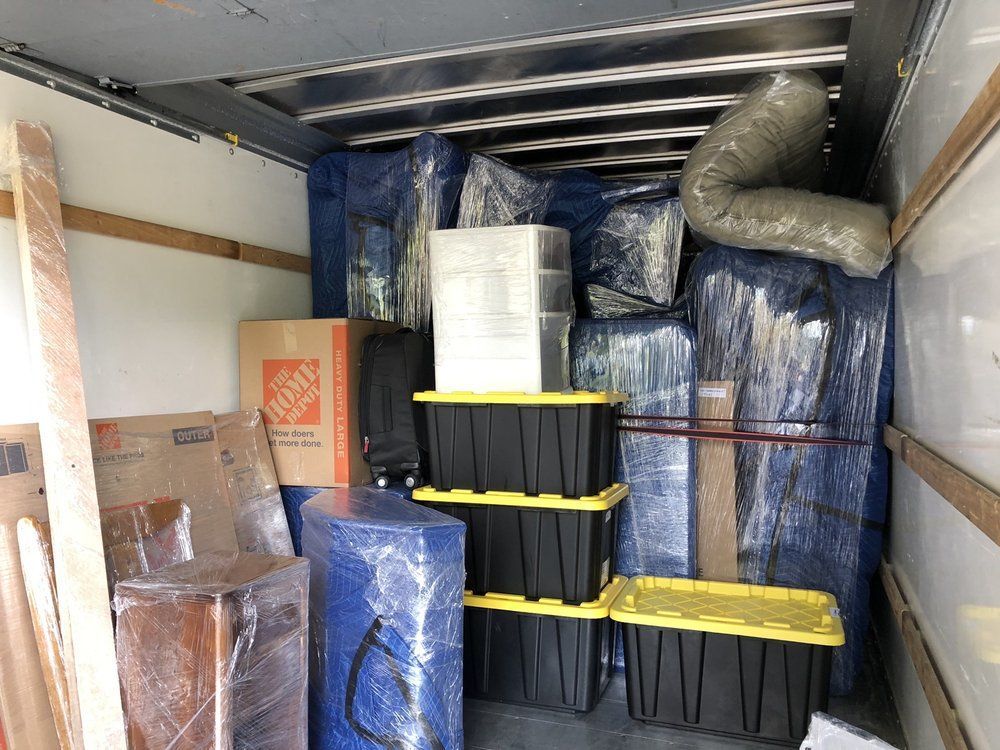 Truck bed filled with furniture and boxes wrapped in blue and clear plastic, ready for transport.