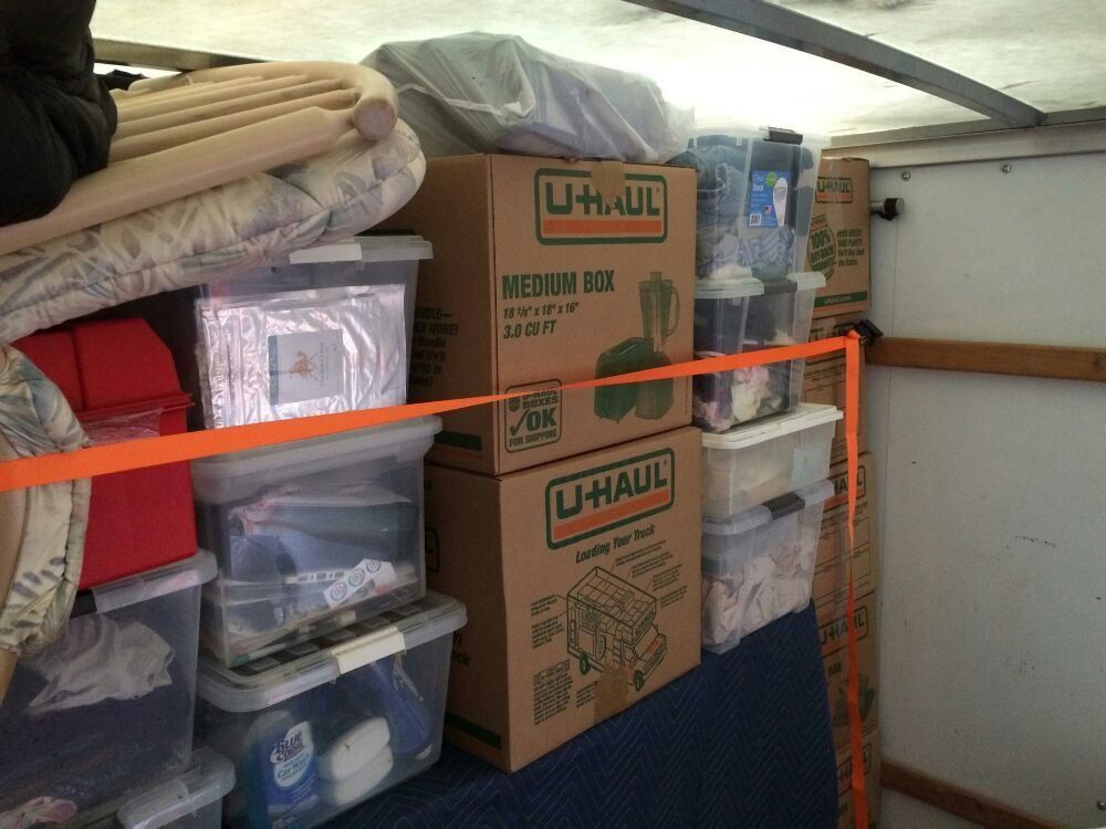 Moving truck interior loaded with boxes and containers, secured with an orange strap.