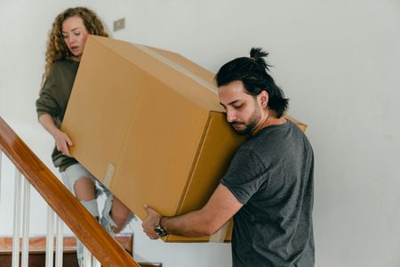 Couple carrying large cardboard box up a flight of stairs.