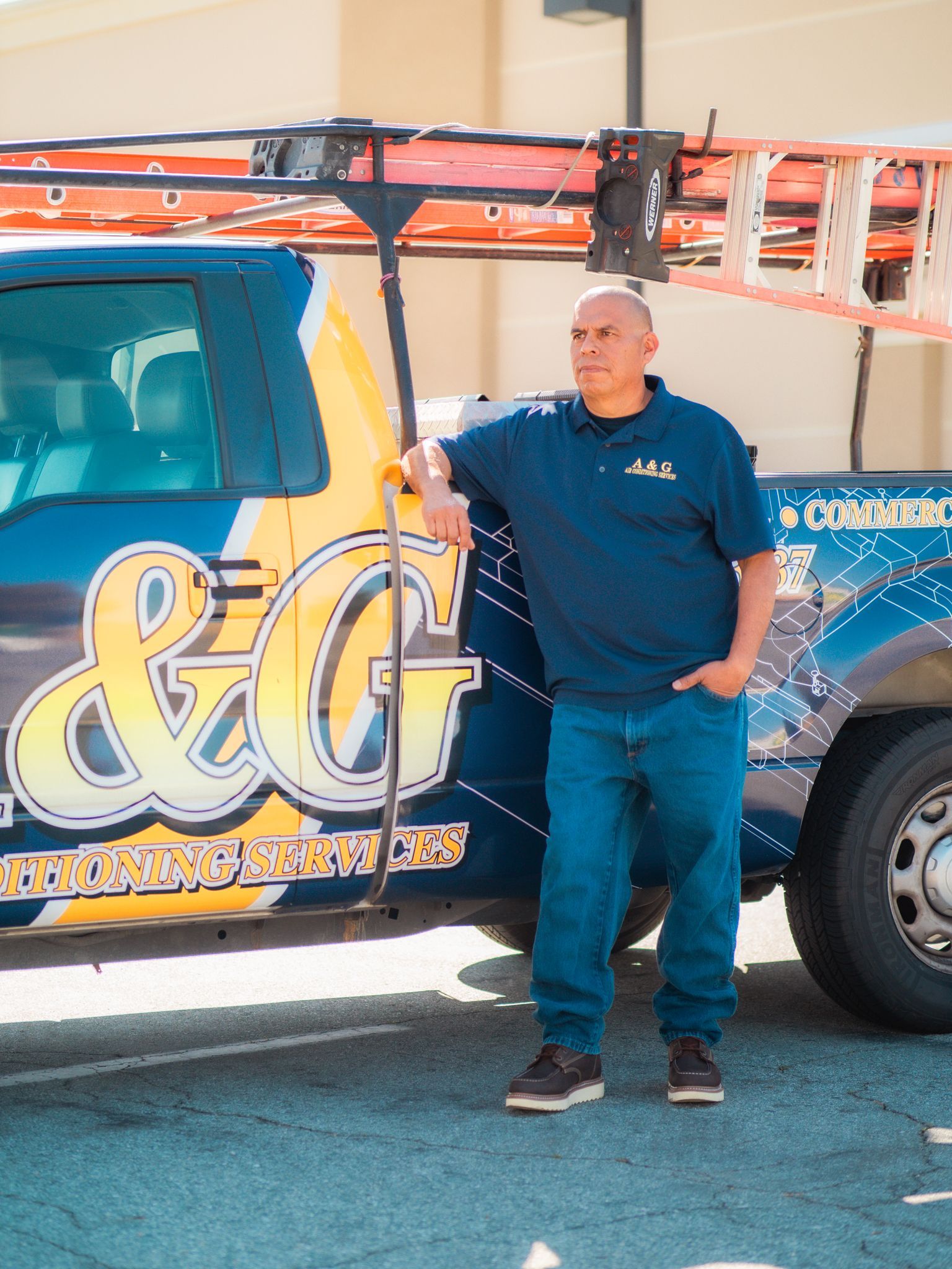 An A & G Technician  is standing next to a truck with a ladder on top of it.