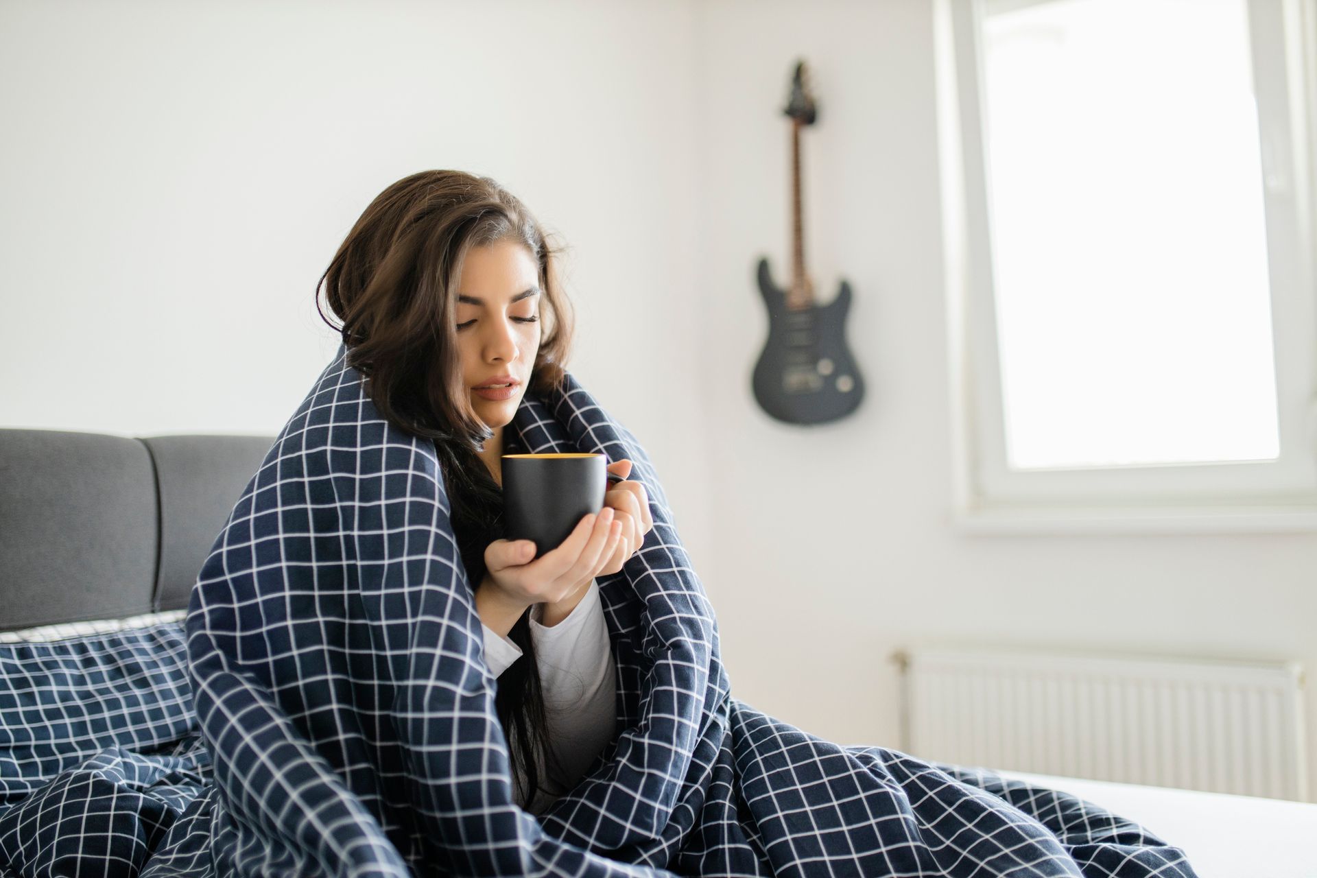 A woman bundled in a blanket and drinking coffee showing an aging furnace with performance issues.
