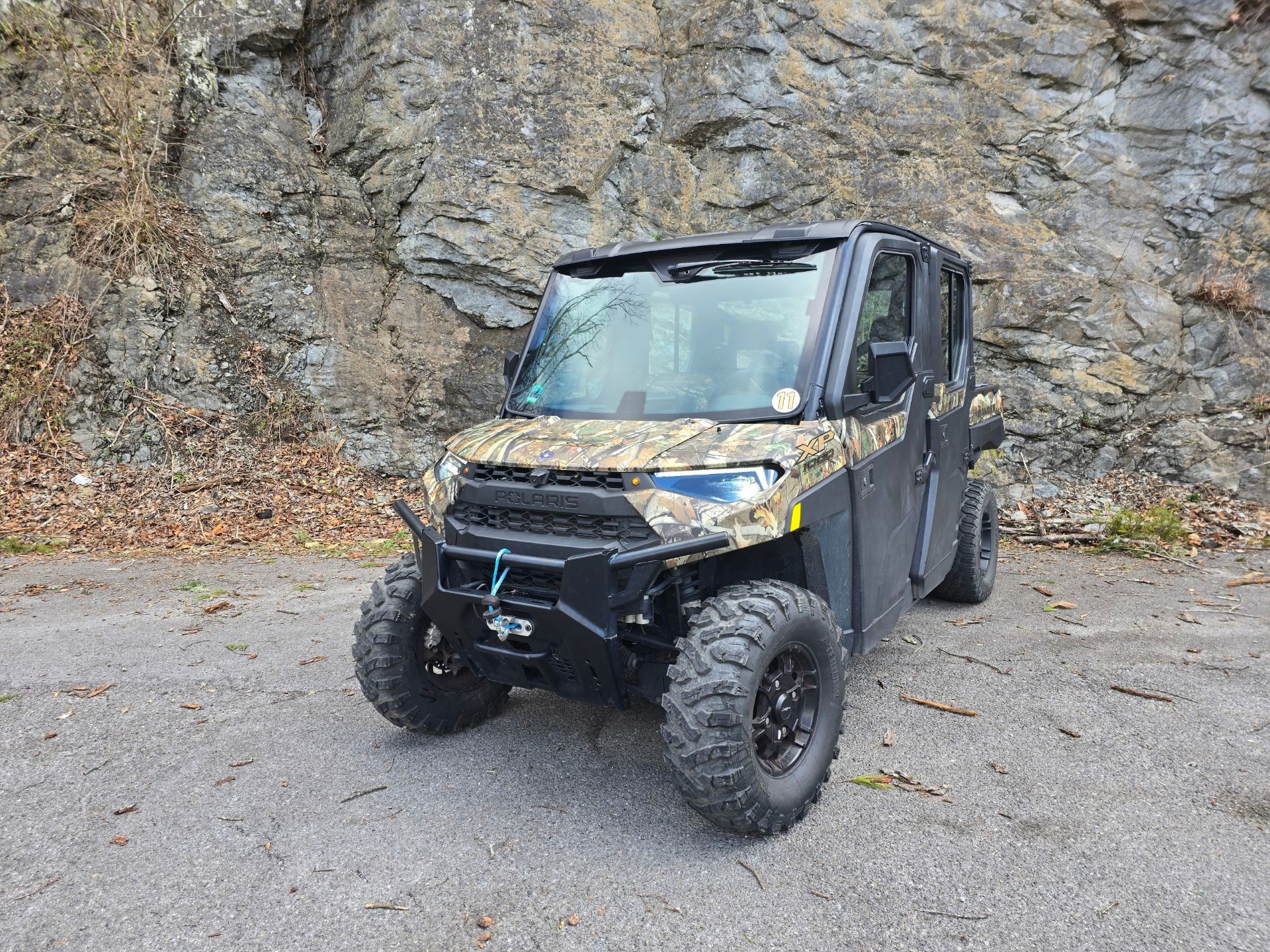 A polaris ranger 1000 is parked on the side of the road in front of a rock wall.