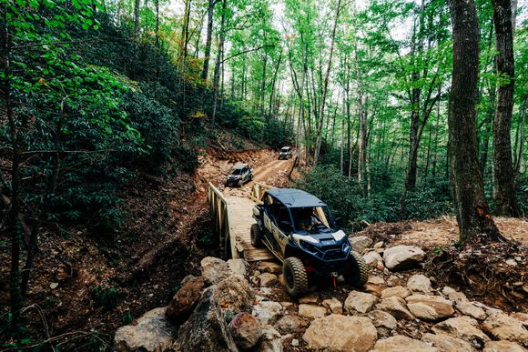 Two atvs are driving down a rocky trail in the woods.