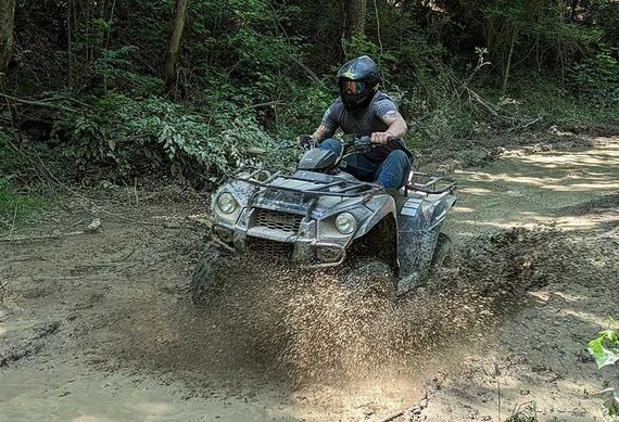 A man is riding a four wheeler through the mud.