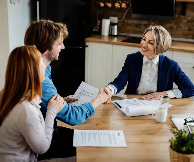 a woman is shaking hands with a man and a woman while sitting at a table