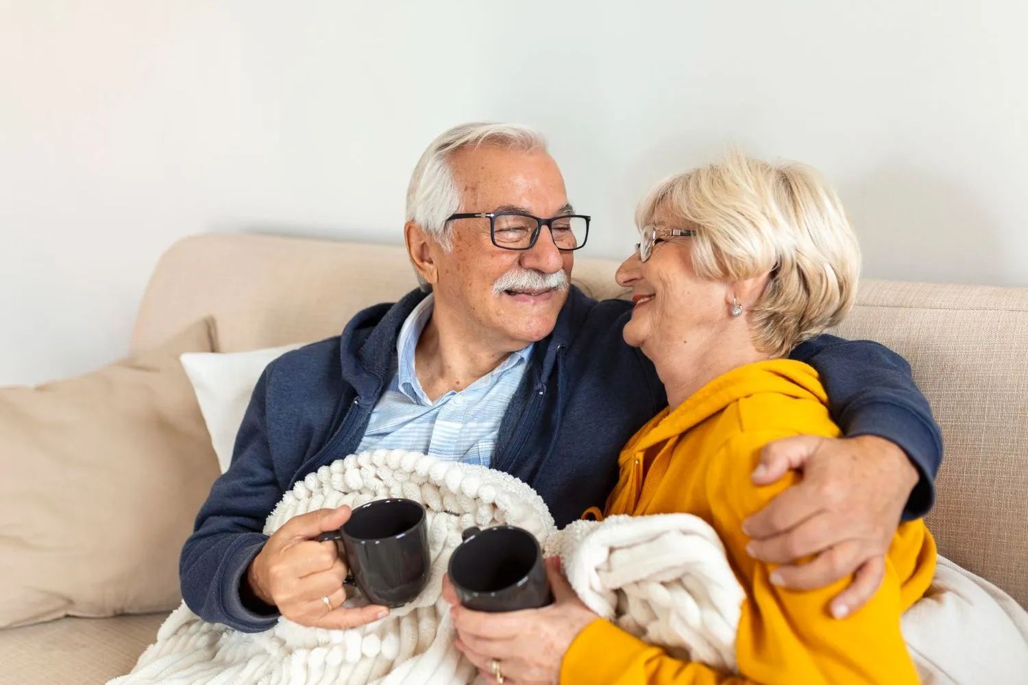 an elderly couple is sitting on a couch holding cups of coffee