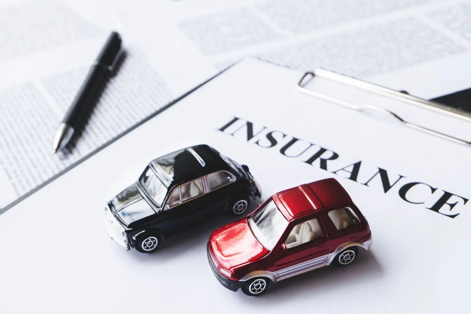 two toy cars are sitting on top of a clipboard with the word insurance written on it