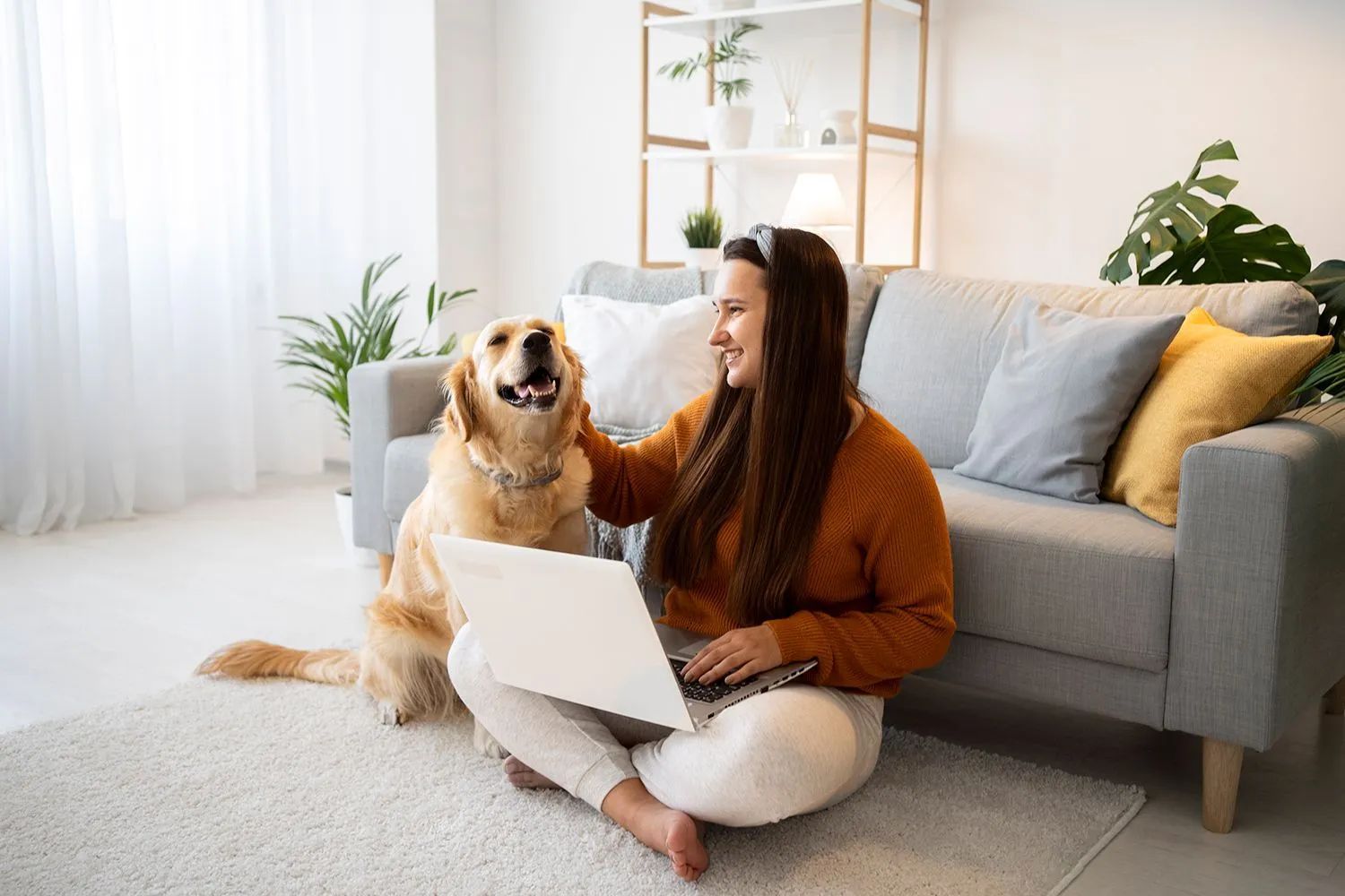 a woman is sitting on the floor with a laptop and petting her dog