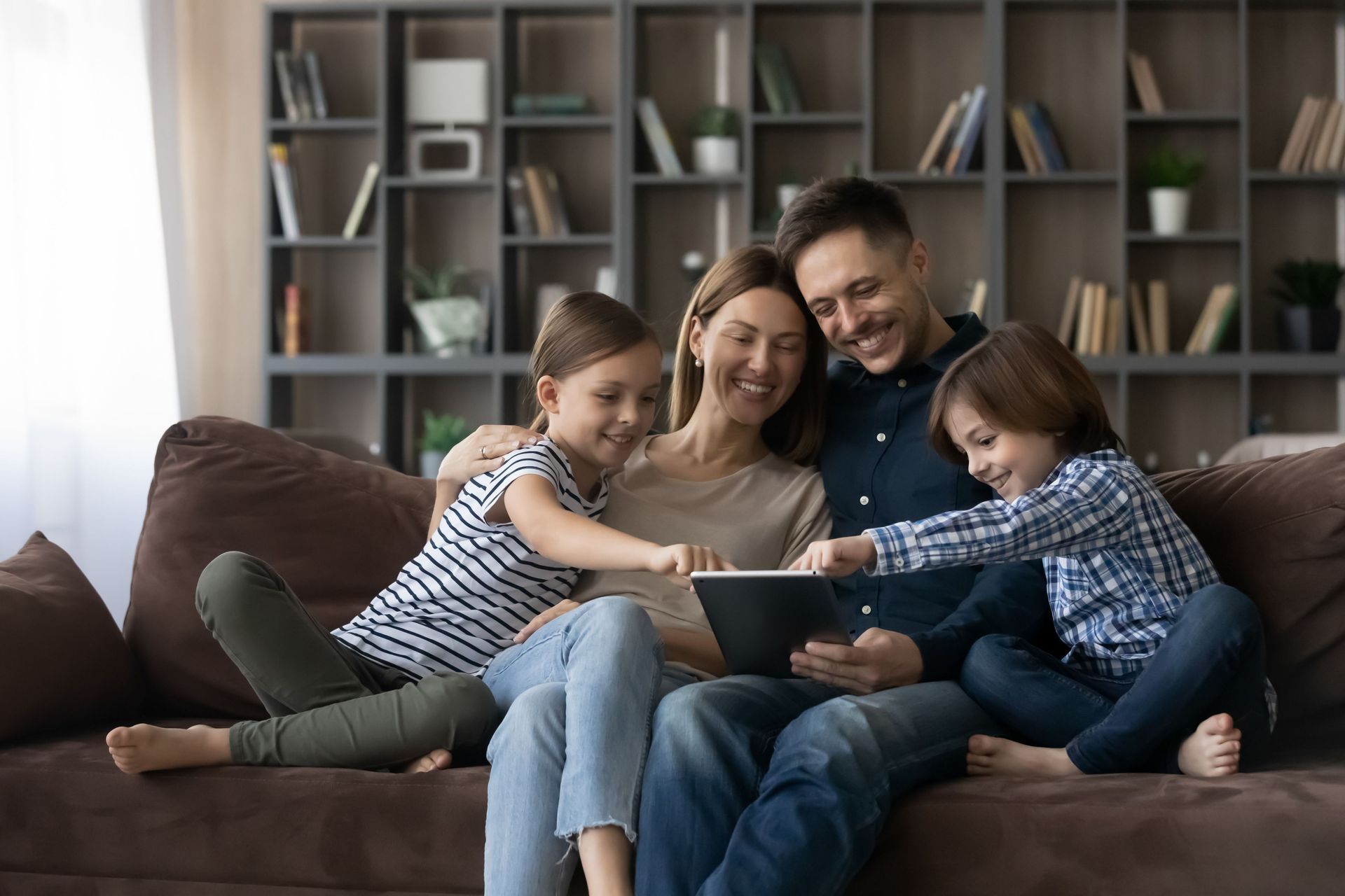 a family is sitting on a couch looking at a tablet