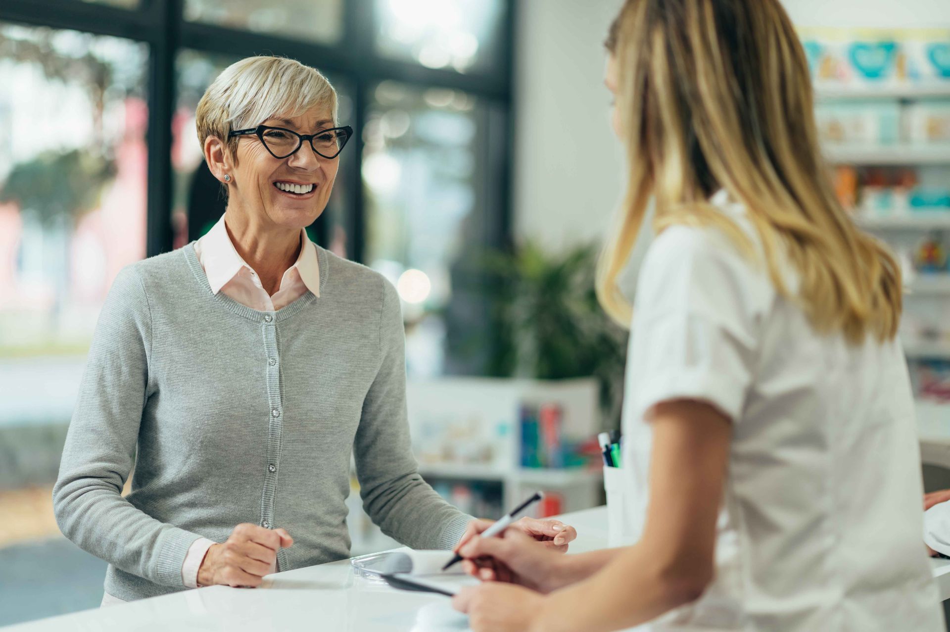 a woman is sitting at a counter in a pharmacy talking to a pharmacist