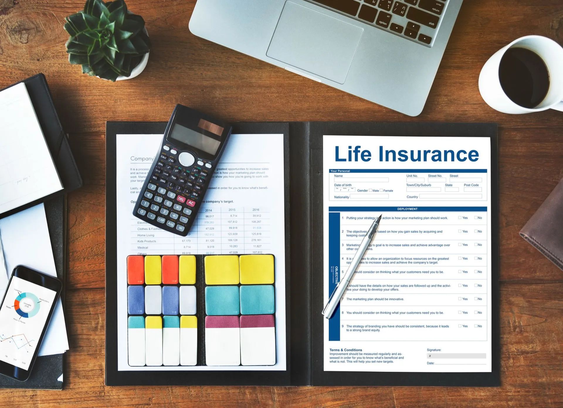 a desk with a laptop , cell phone , calculator , and a life insurance form